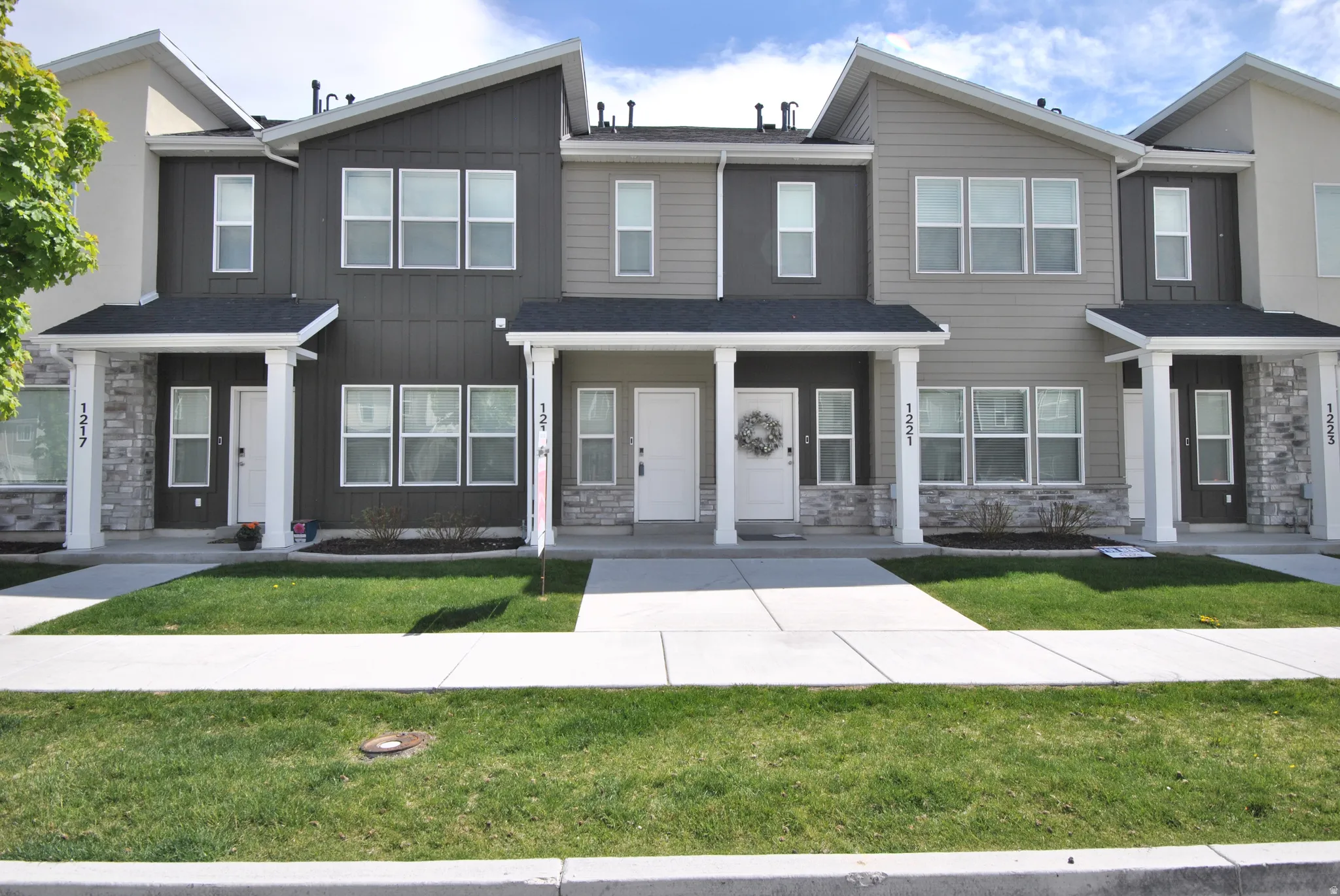 Contemporary townhome facade featuring a dark gray and light gray color palette, white trim, stone veneer accents, and multiple large windows