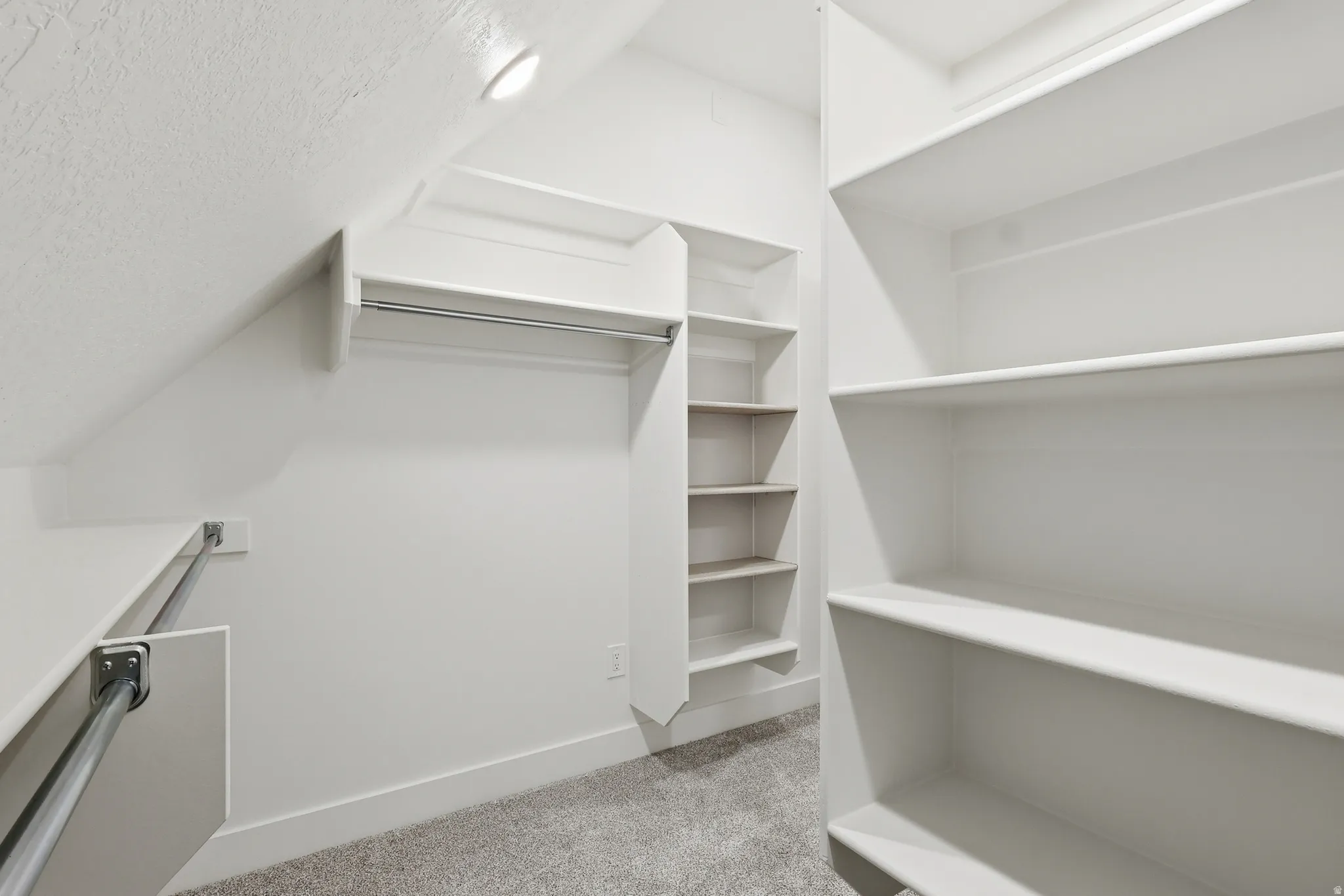 Master suite walk in closet featuring light carpet and vaulted ceiling