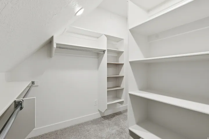 Master suite walk in closet featuring light carpet and vaulted ceiling