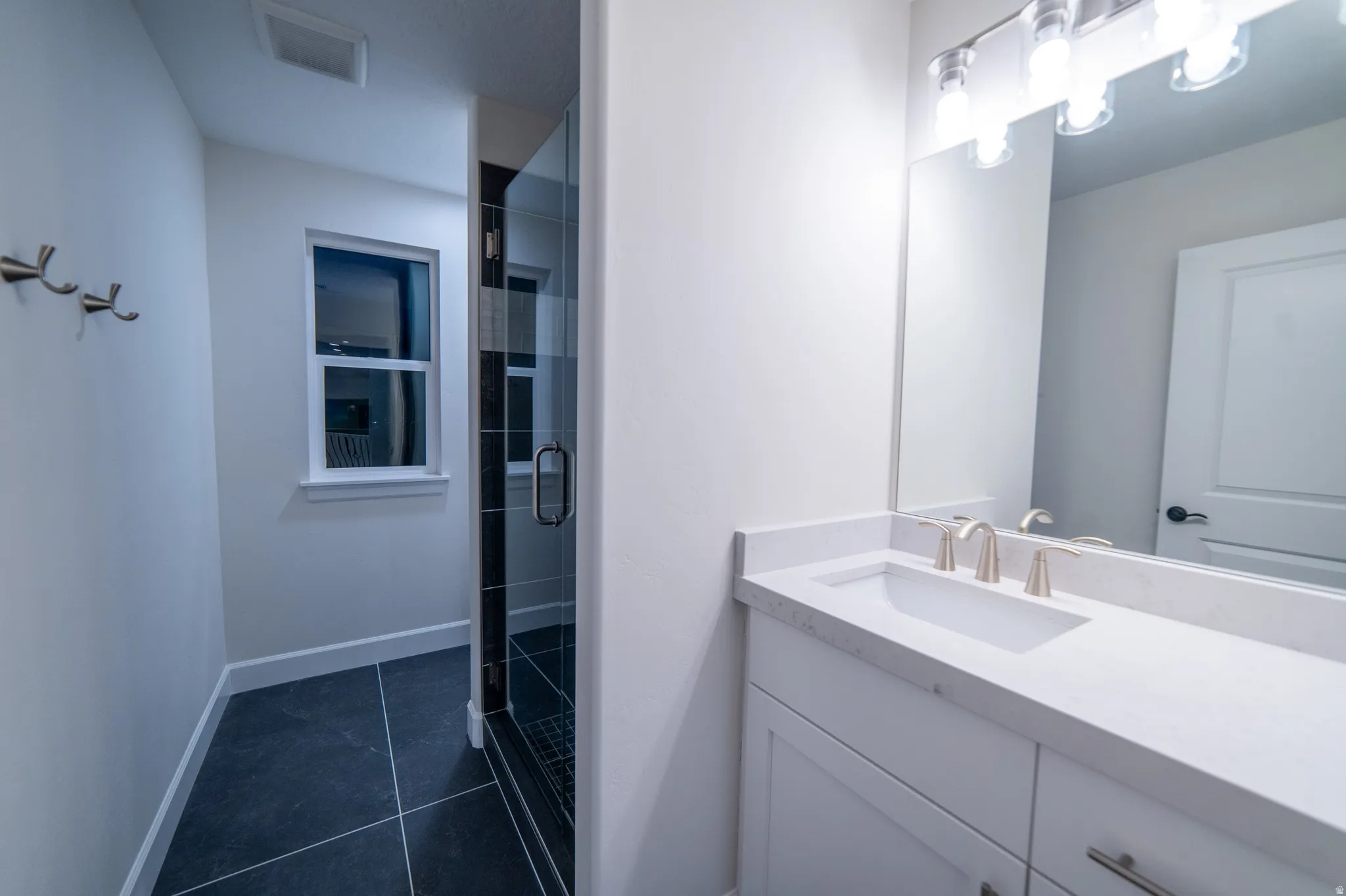 Full bathroom featuring a stall shower, vanity, and dark tile patterned flooring