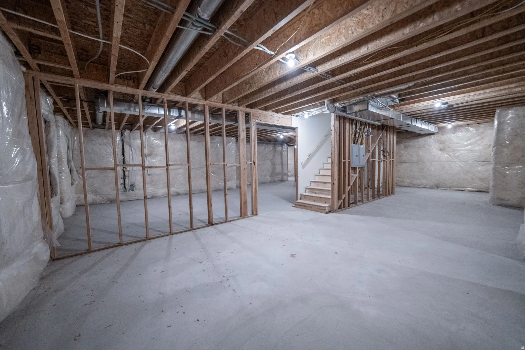 Unfinished basement featuring stairs and electric panel