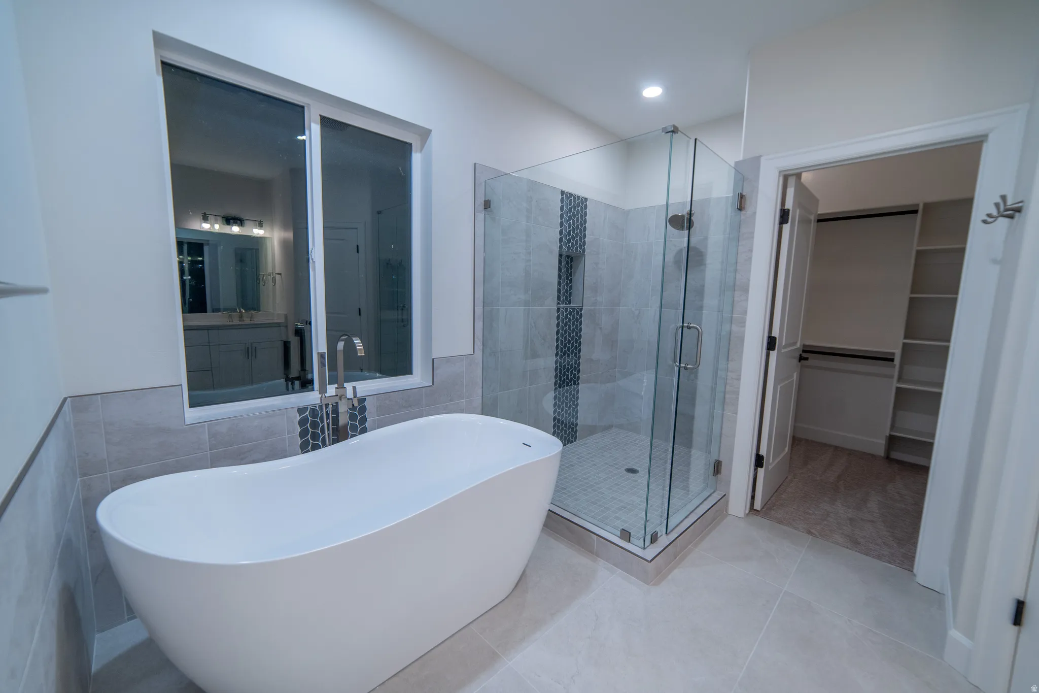 Bathroom featuring a shower stall, a spacious closet, tile walls, a freestanding bath, and tile patterned floors