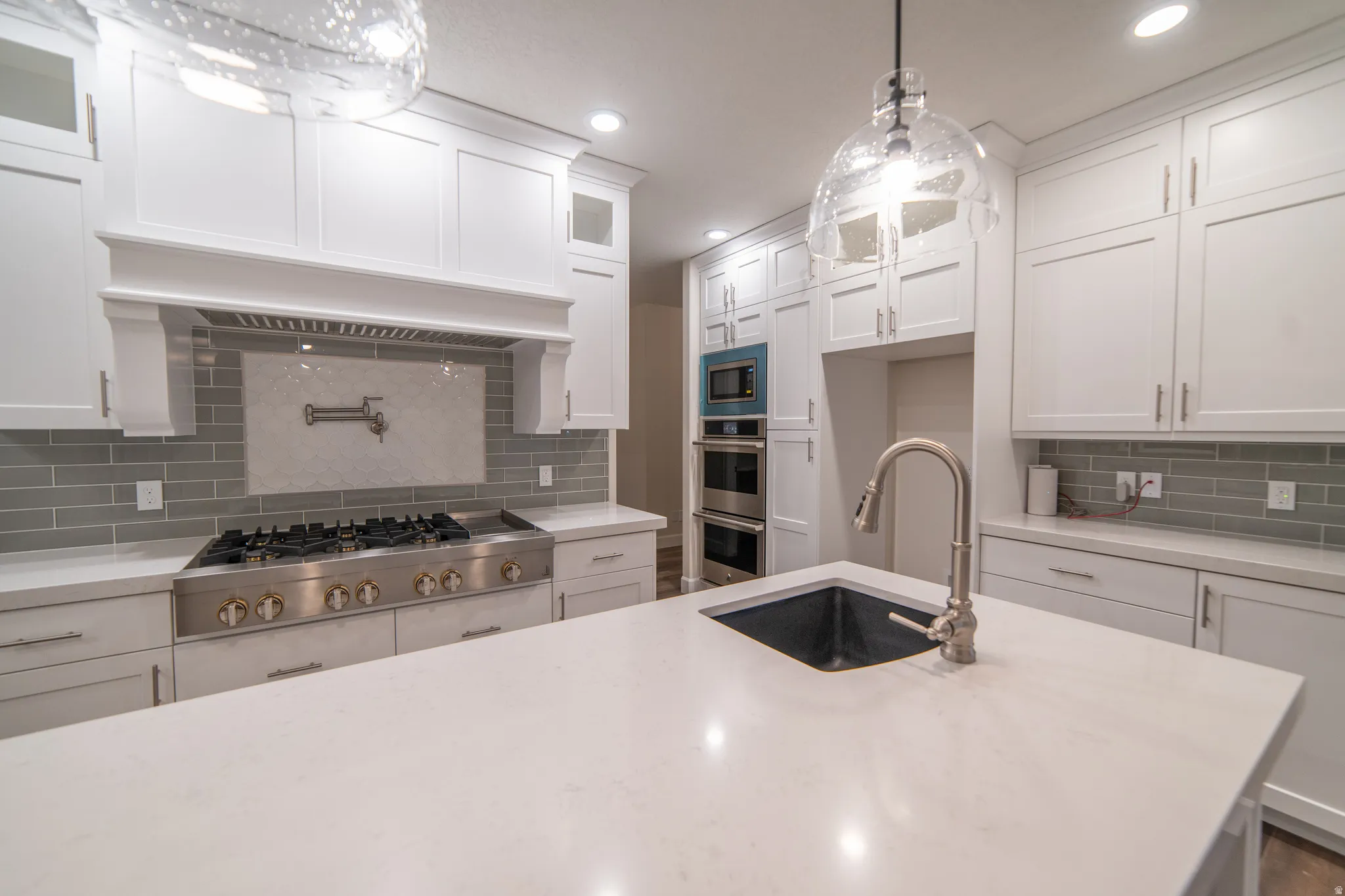 Kitchen featuring tasteful backsplash, white cabinets, glass insert cabinets, appliances with stainless steel finishes, and light stone countertops