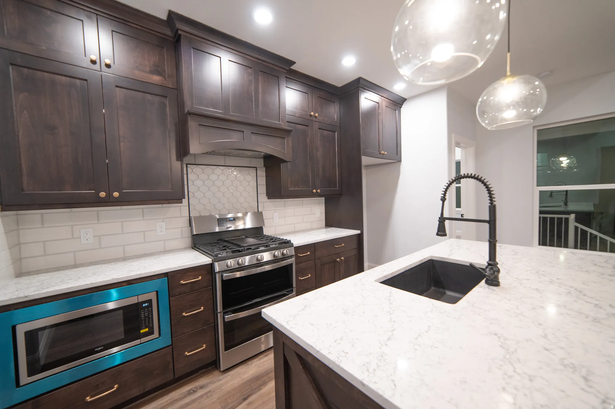 Kitchen featuring dark brown cabinets, appliances with stainless steel finishes, backsplash, light stone counters, and recessed lighting
