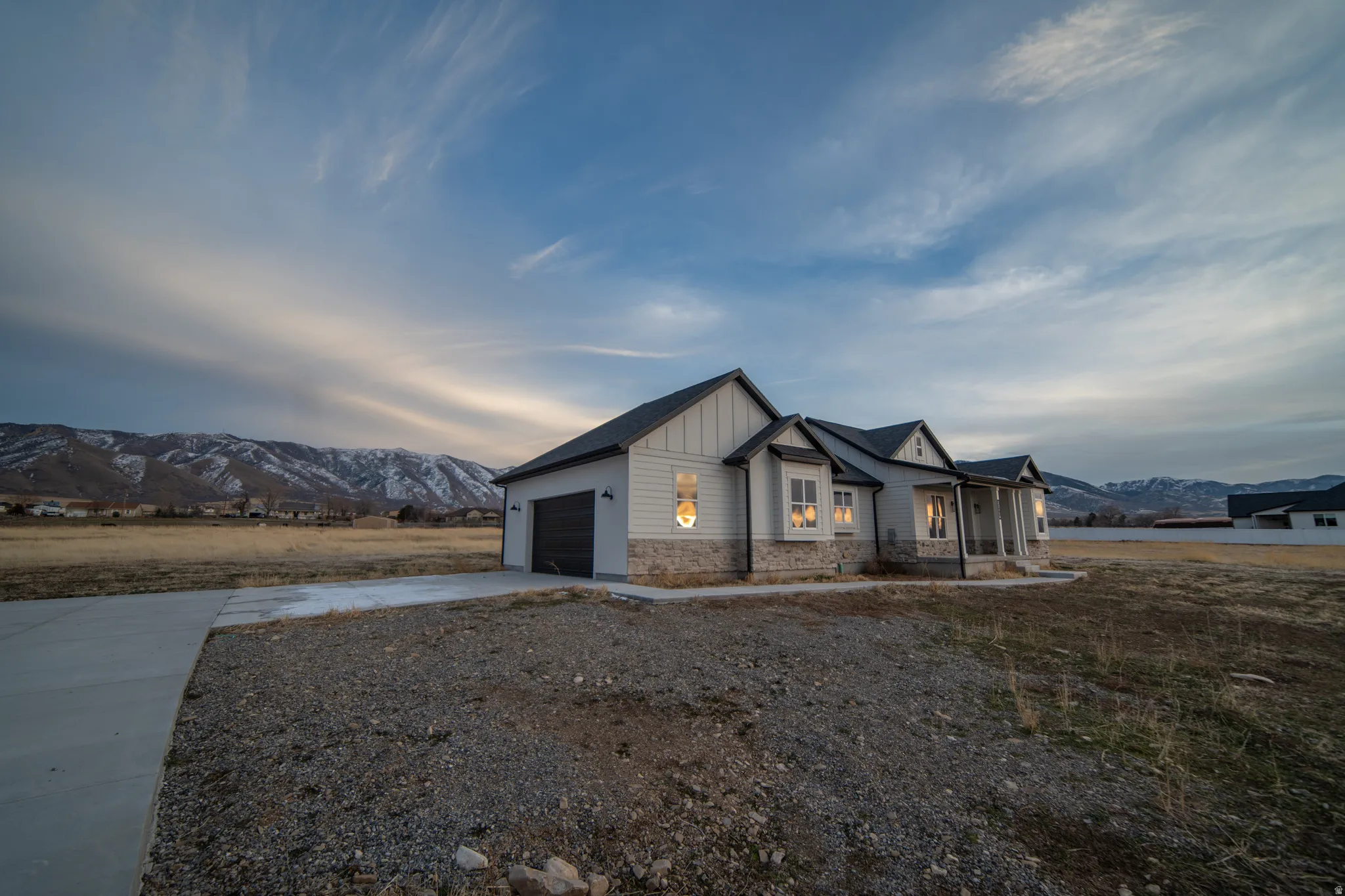 Modern farmhouse style home featuring a mountain view, board and batten siding, a porch, concrete driveway, and stone siding