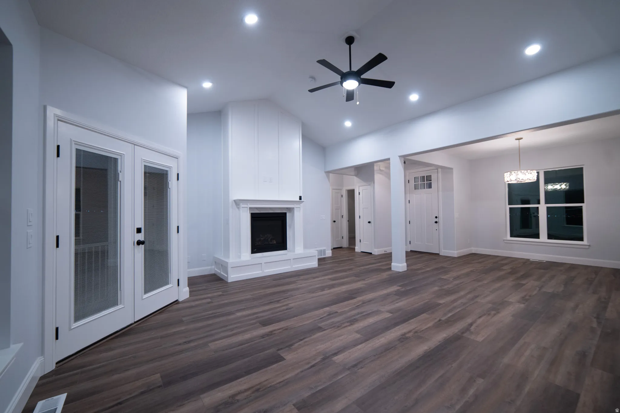 Unfurnished living room with a fireplace with raised hearth, dark wood-style floors, ceiling fan, lofted ceiling, and french doors