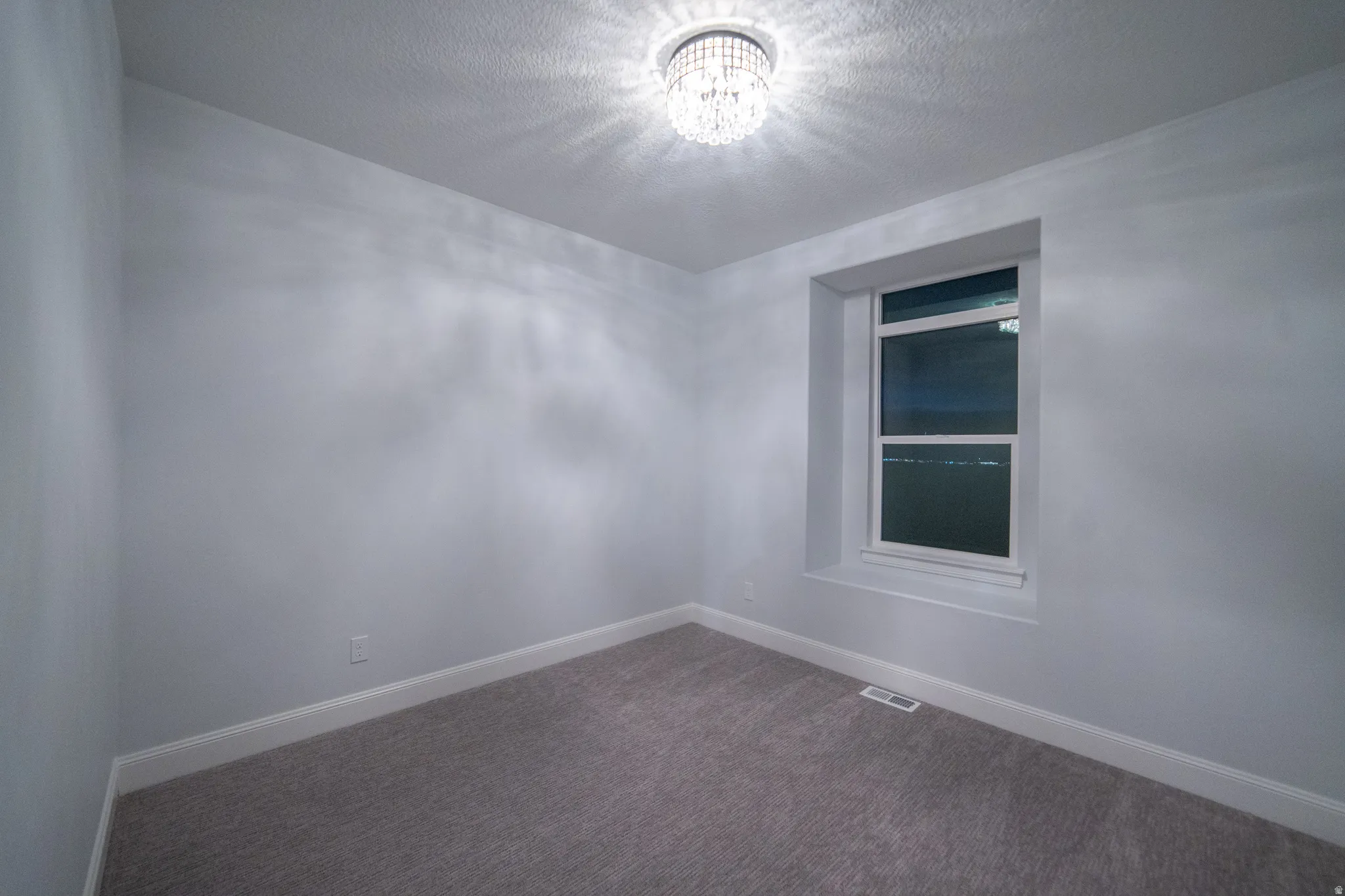 Carpeted empty room featuring a textured ceiling and a chandelier