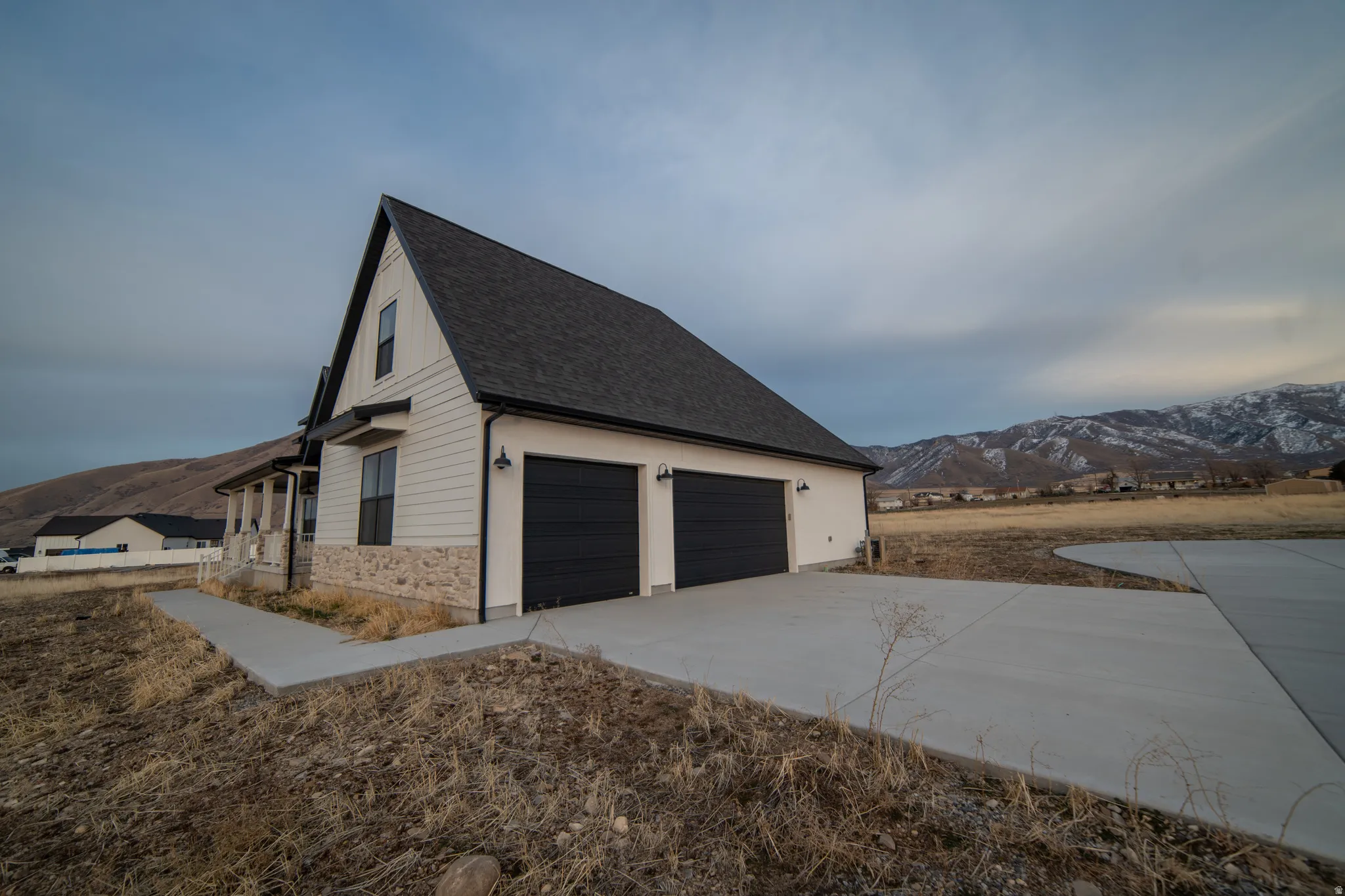 View of side of home with a mountain view, a shingled roof, a garage, and driveway
