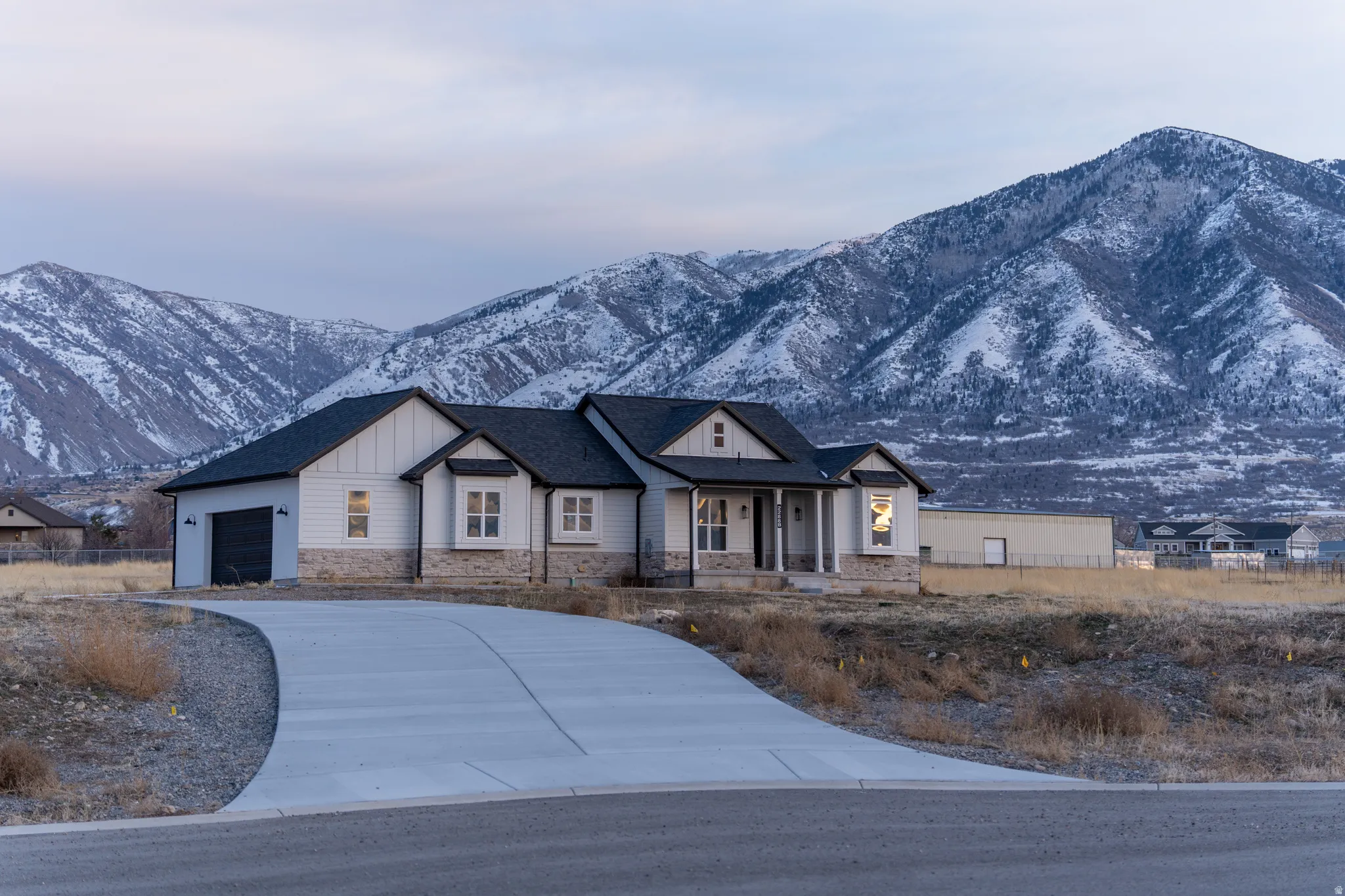 Modern farmhouse style home featuring stone siding, a porch, driveway, board and batten siding, and a garage