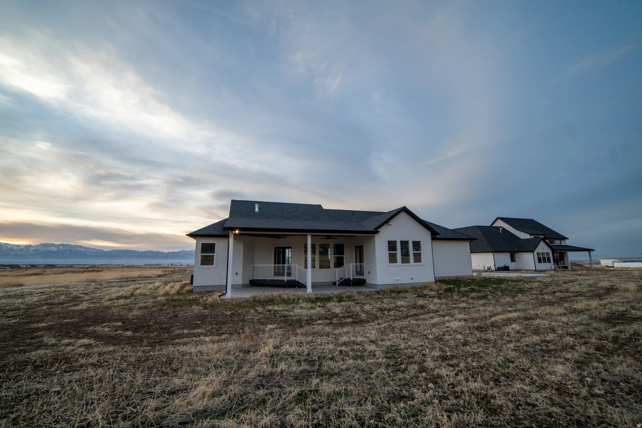 Back of house at dusk with a patio, ceiling fan, a shingled roof, and a mountain view