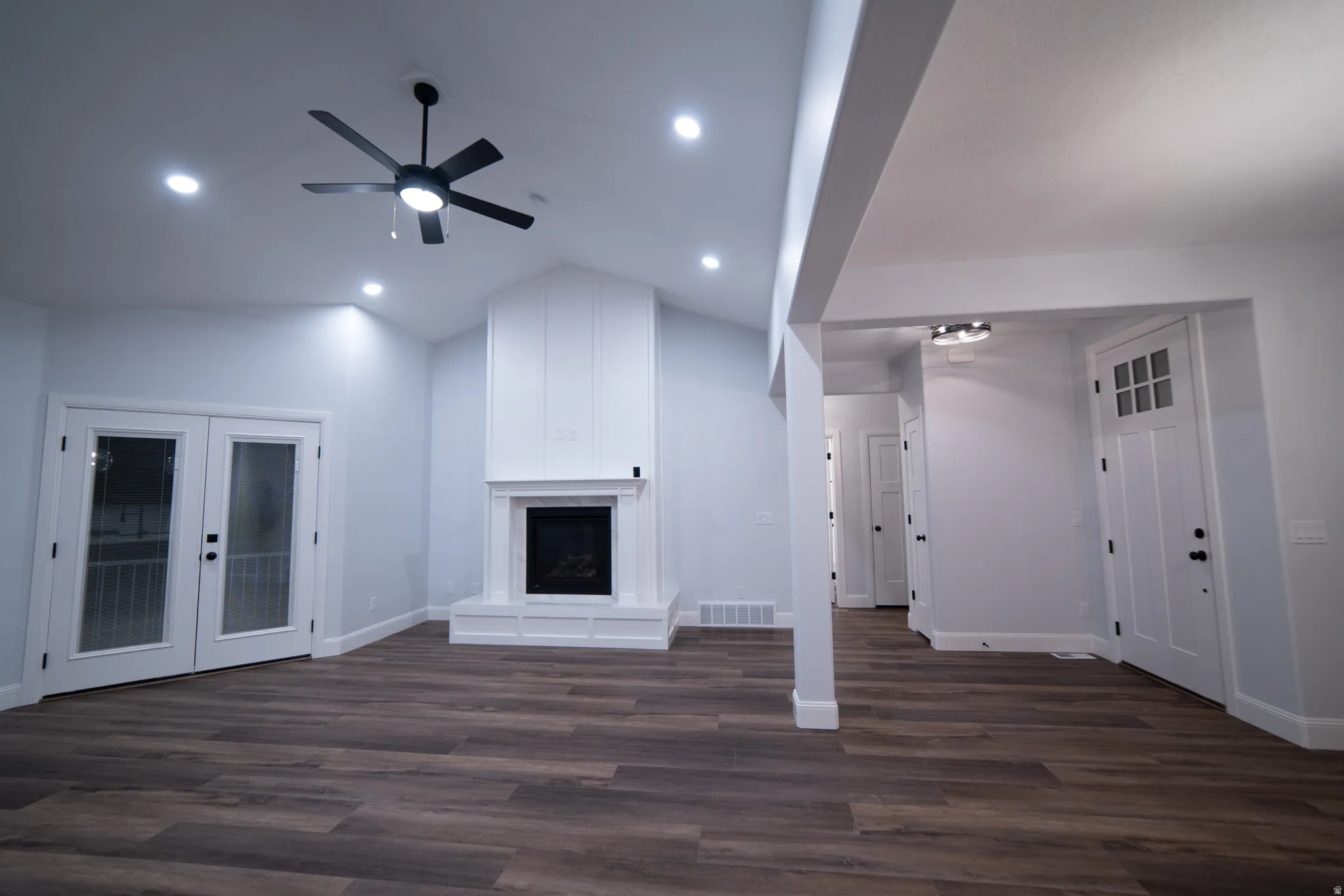 Unfurnished living room with a fireplace with raised hearth, french doors, dark wood-type flooring, lofted ceiling, and ceiling fan