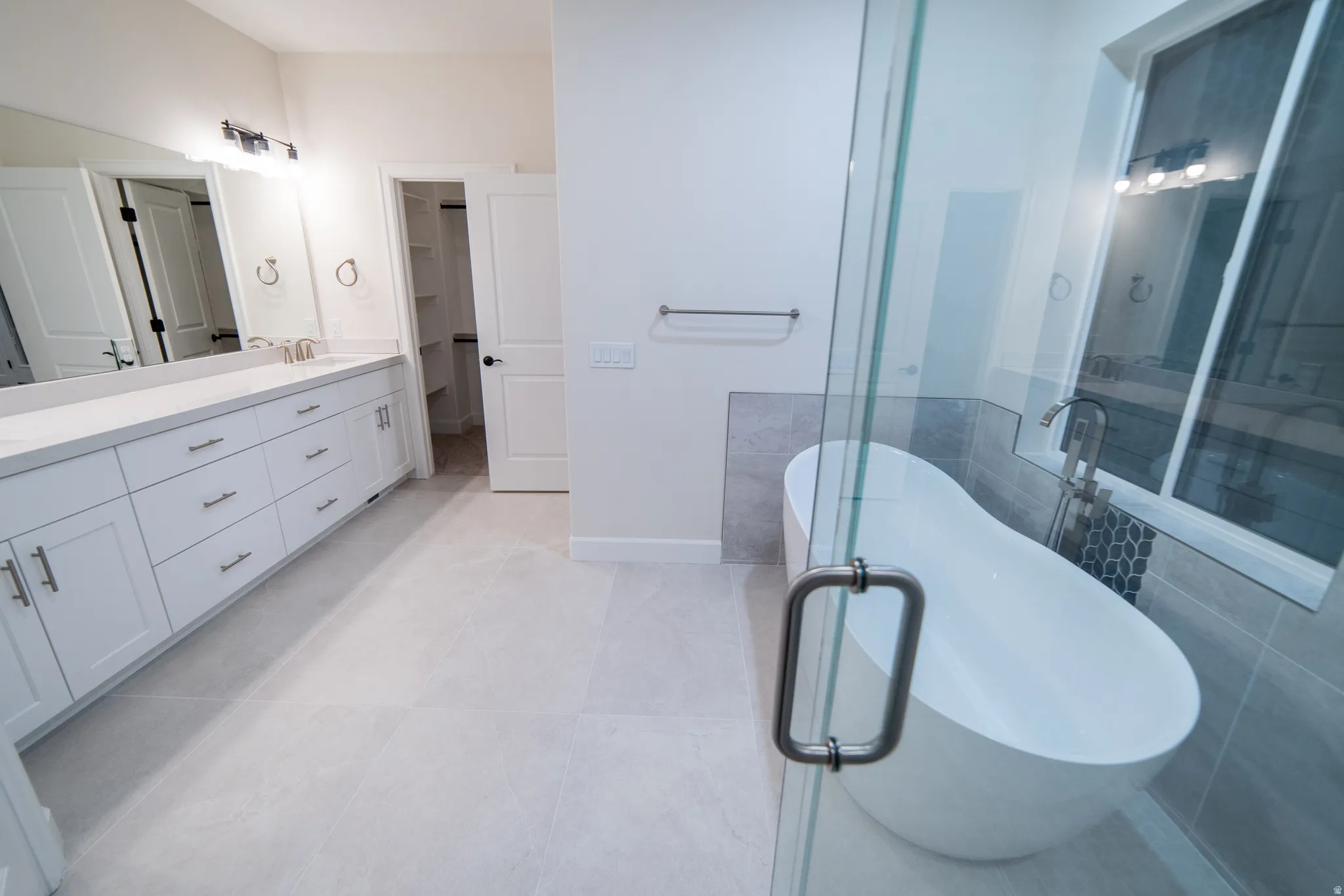 Bathroom featuring double vanity, a spacious closet, a soaking tub, and light tile patterned floors