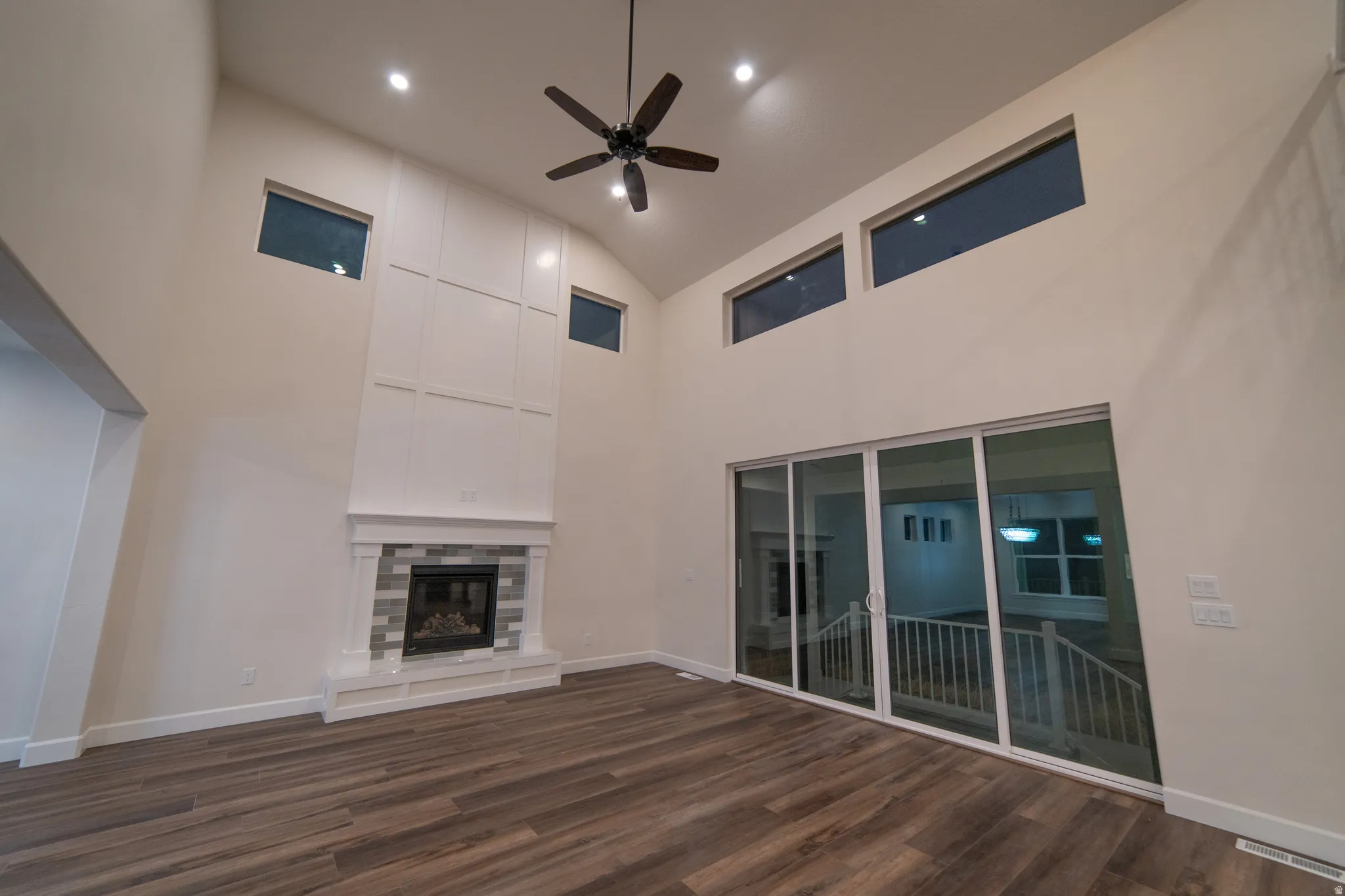 Unfurnished living room with ceiling fan, a glass covered fireplace, dark wood finished floors, recessed lighting, and high vaulted ceiling