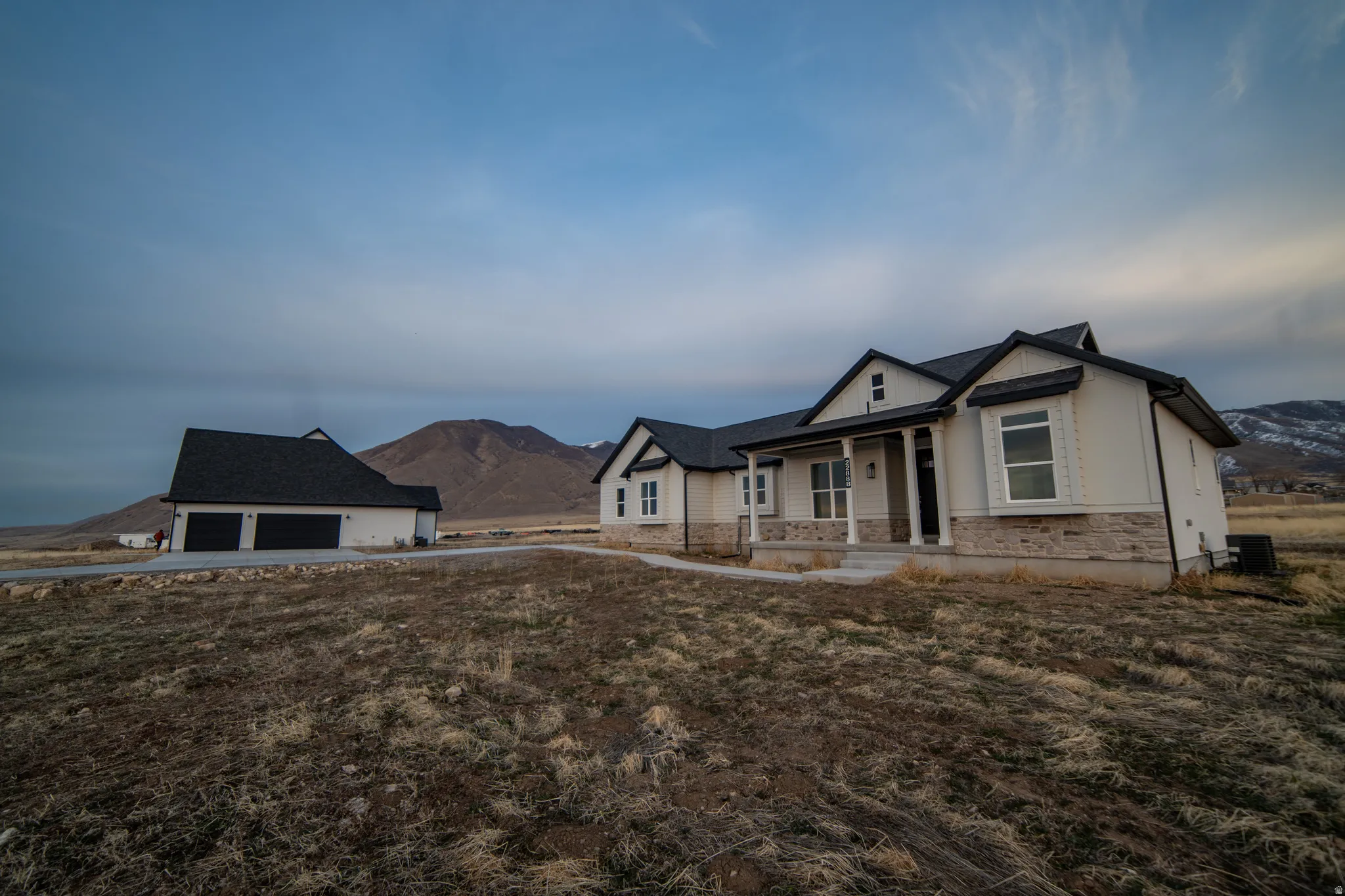 View of front of home featuring a mountain view, a porch, an outbuilding, stone siding, and a garage