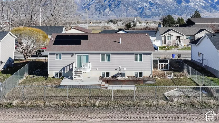 Rear view of property featuring roof mounted solar panels, a fenced backyard, a shingled roof, a mountain view, and a residential view