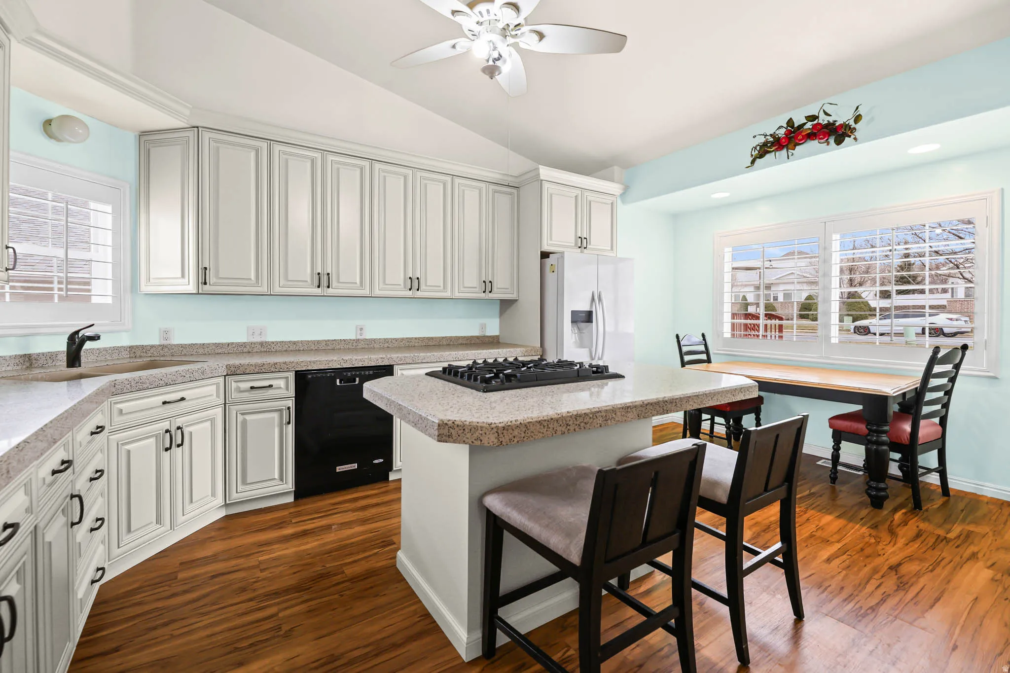 Kitchen with light countertops, white fridge with ice dispenser, black dishwasher, vaulted ceiling, and a kitchen island
