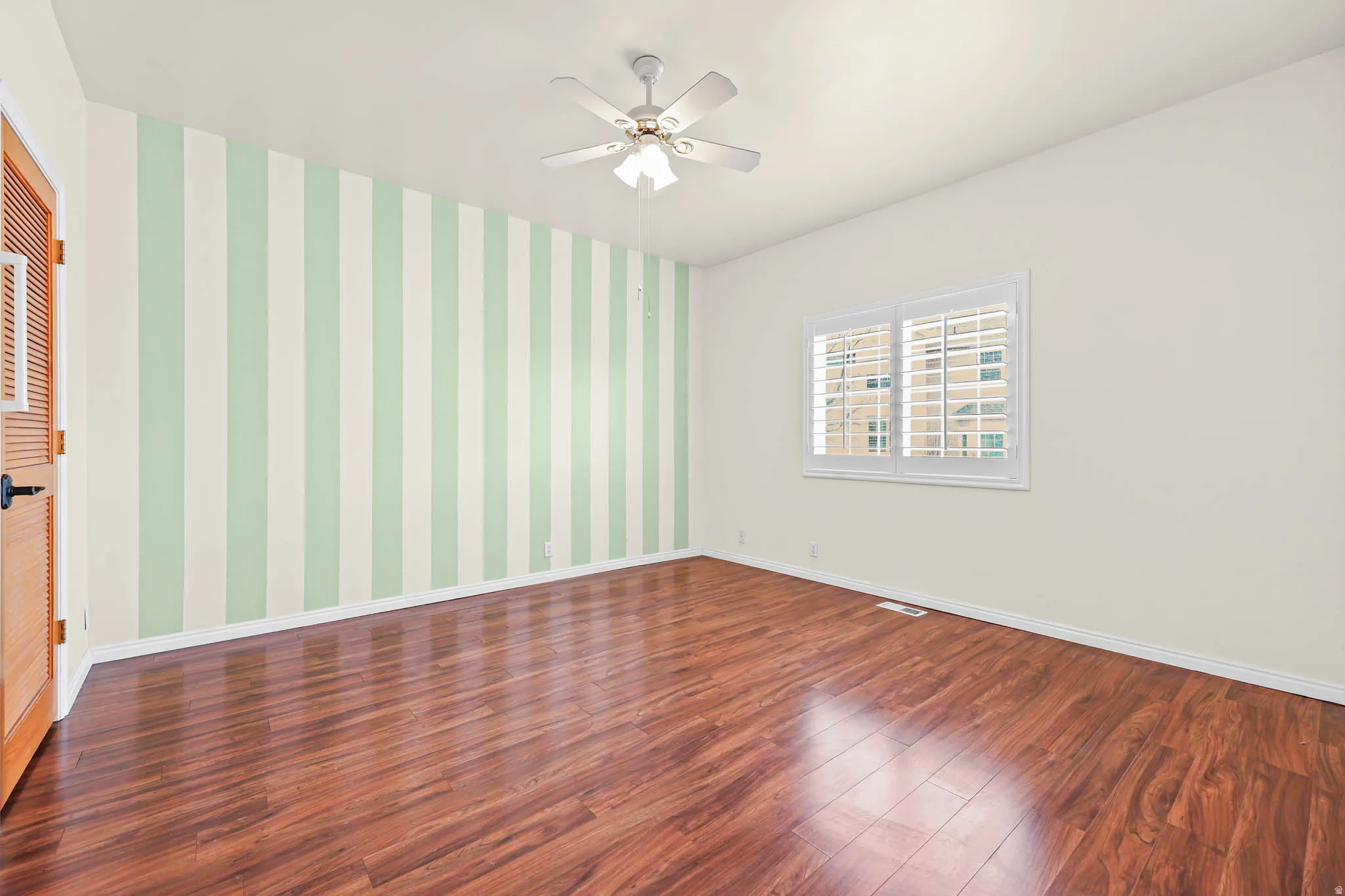 Empty room featuring wallpapered walls, dark wood-style flooring, and ceiling fan