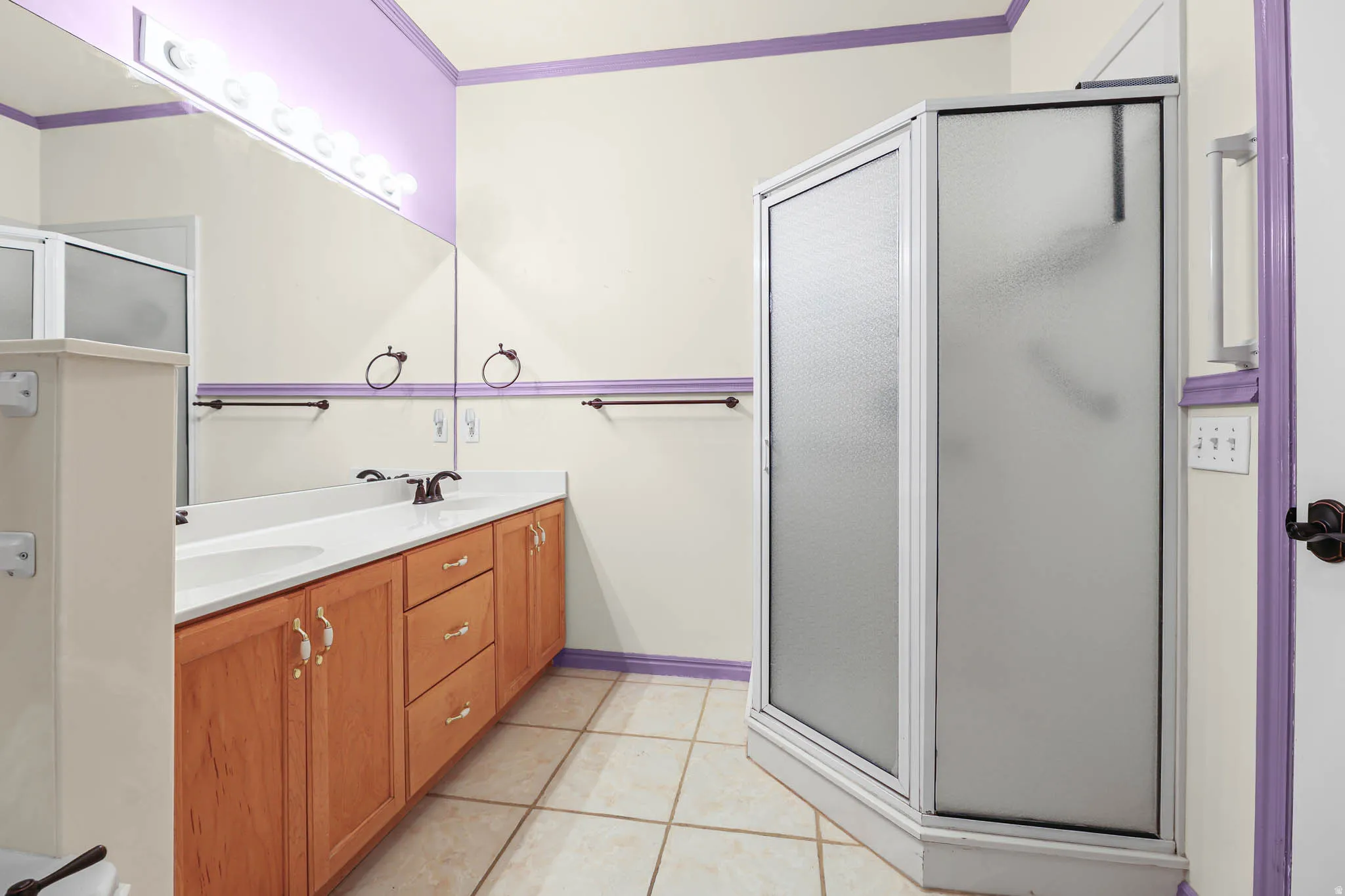 Bathroom featuring a stall shower, double vanity, crown molding, and light tile patterned floors