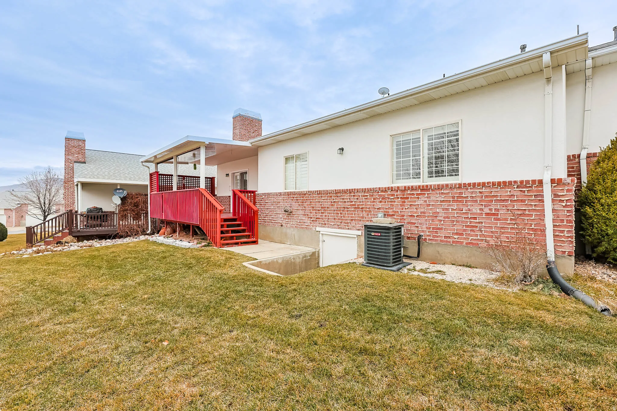 Rear view of house with brick siding, a yard, a deck, a chimney, and stucco siding