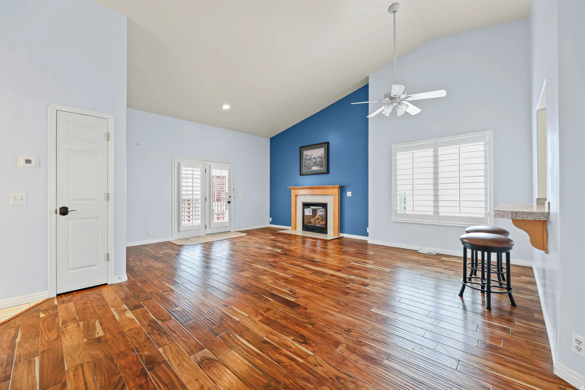 Unfurnished living room featuring high vaulted ceiling, a fireplace with flush hearth, dark wood-style flooring, and a ceiling fan