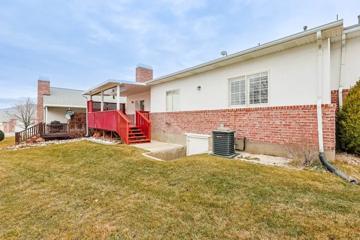 Rear view of house with brick siding, a yard, a deck, a chimney, and stucco siding