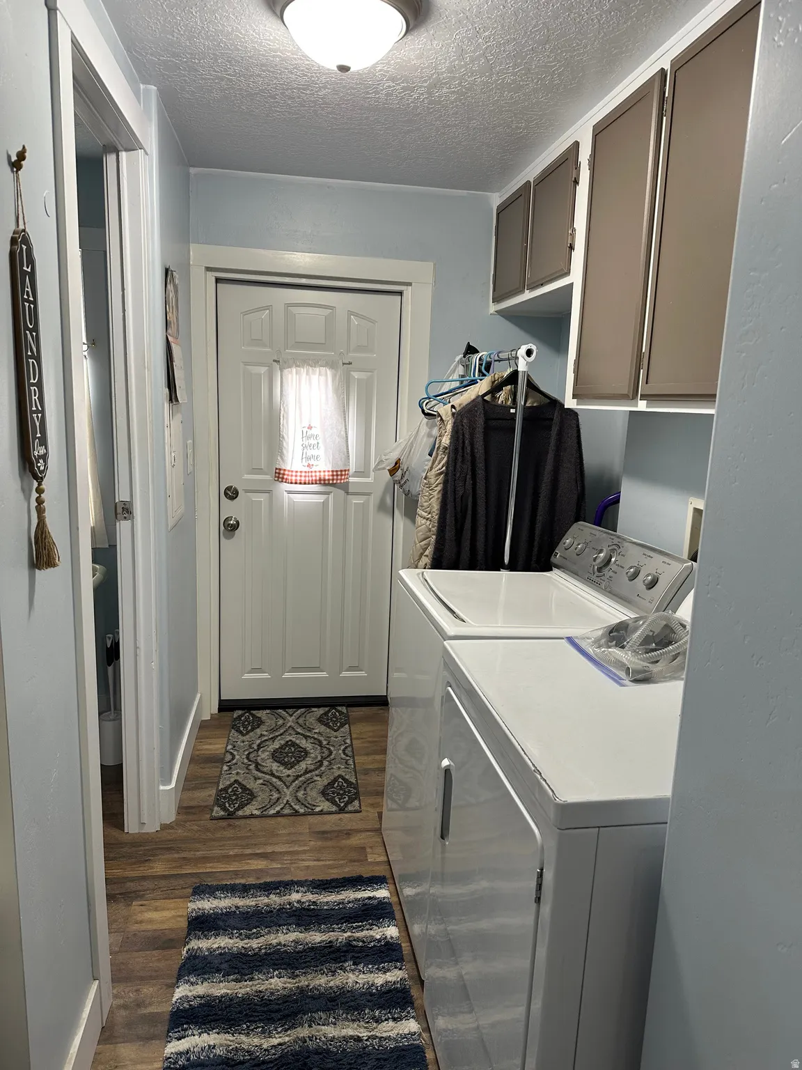 Laundry area with a textured ceiling, cabinet space, dark wood-style floors, and washer and clothes dryer