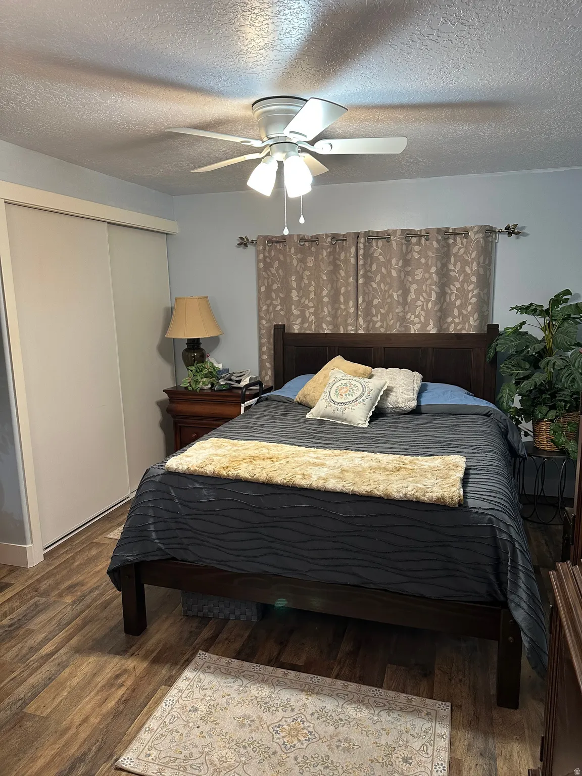 Bedroom with a textured ceiling, a closet, a ceiling fan, and dark wood finished floors