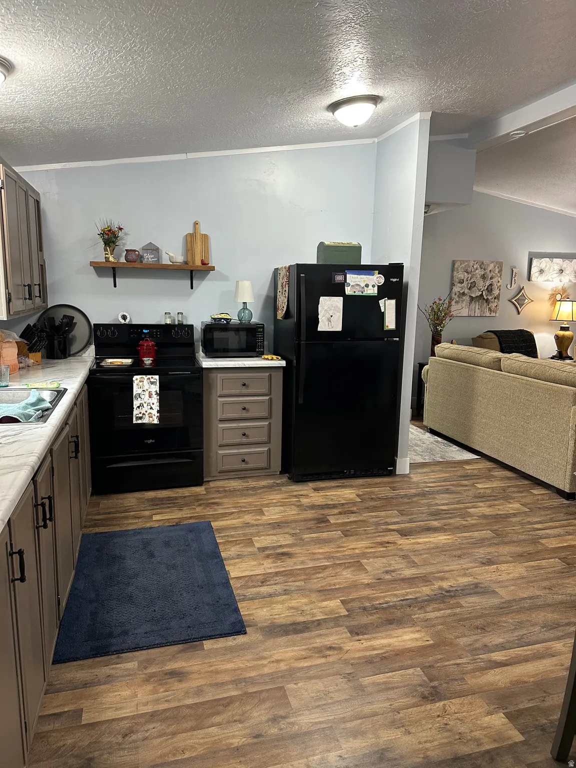 Kitchen with light countertops, a textured ceiling, black appliances, open floor plan, and dark wood-style flooring