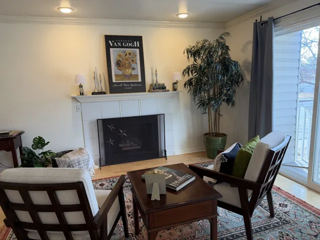 Living room with a tile fireplace, wood finished floors, and ornamental molding