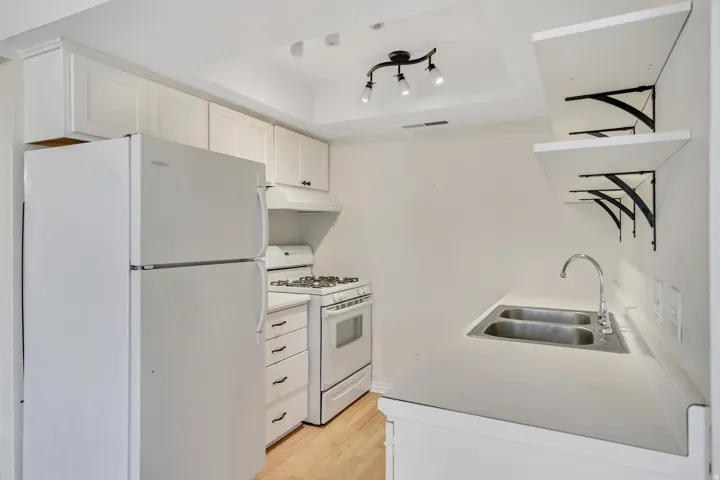 Kitchen with white appliances, white cabinetry, light countertops, a raised ceiling, and under cabinet range hood