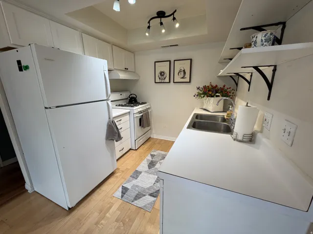 Kitchen featuring a raised ceiling, white appliances, white cabinets, light wood finished floors, and light countertops