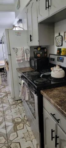 Kitchen featuring electric range, dark countertops, cabinets, light flooring, and black microwave