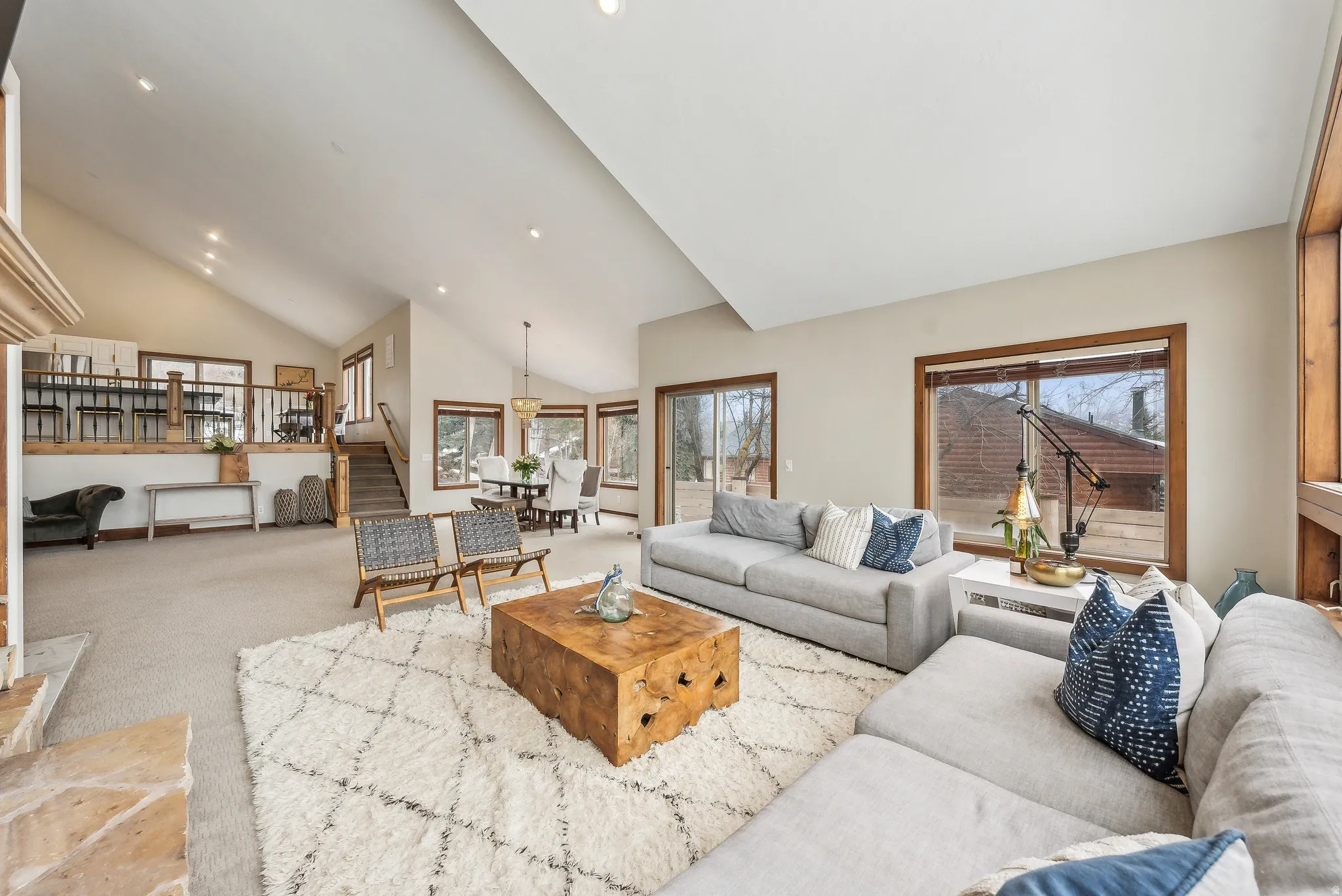 Carpeted living area with healthy amount of natural light, recessed lighting, high vaulted ceiling, and stairway