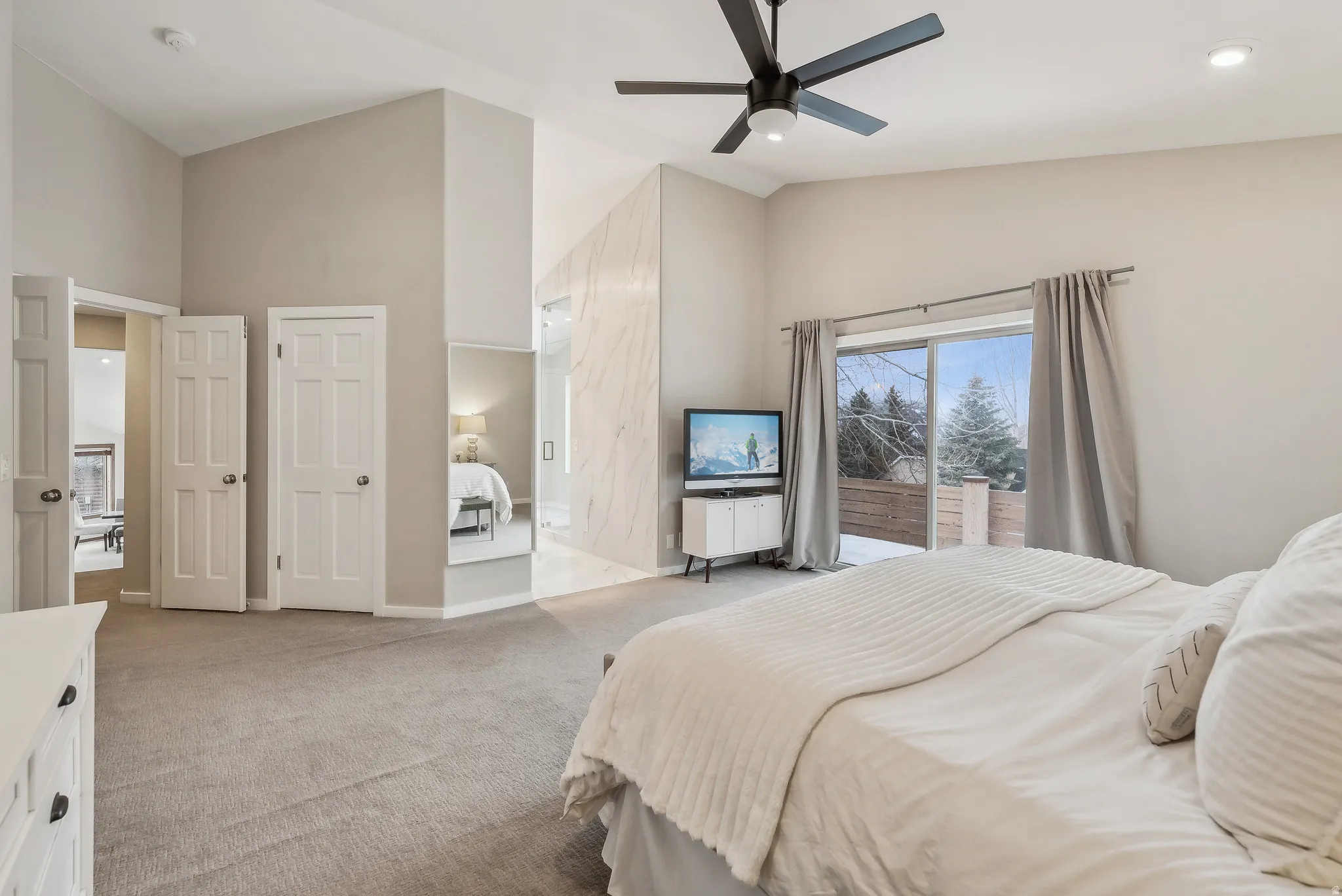 Vaulted ceilings, a contemporary ceiling fan, plush carpeting, and a sliding glass door with outdoor access