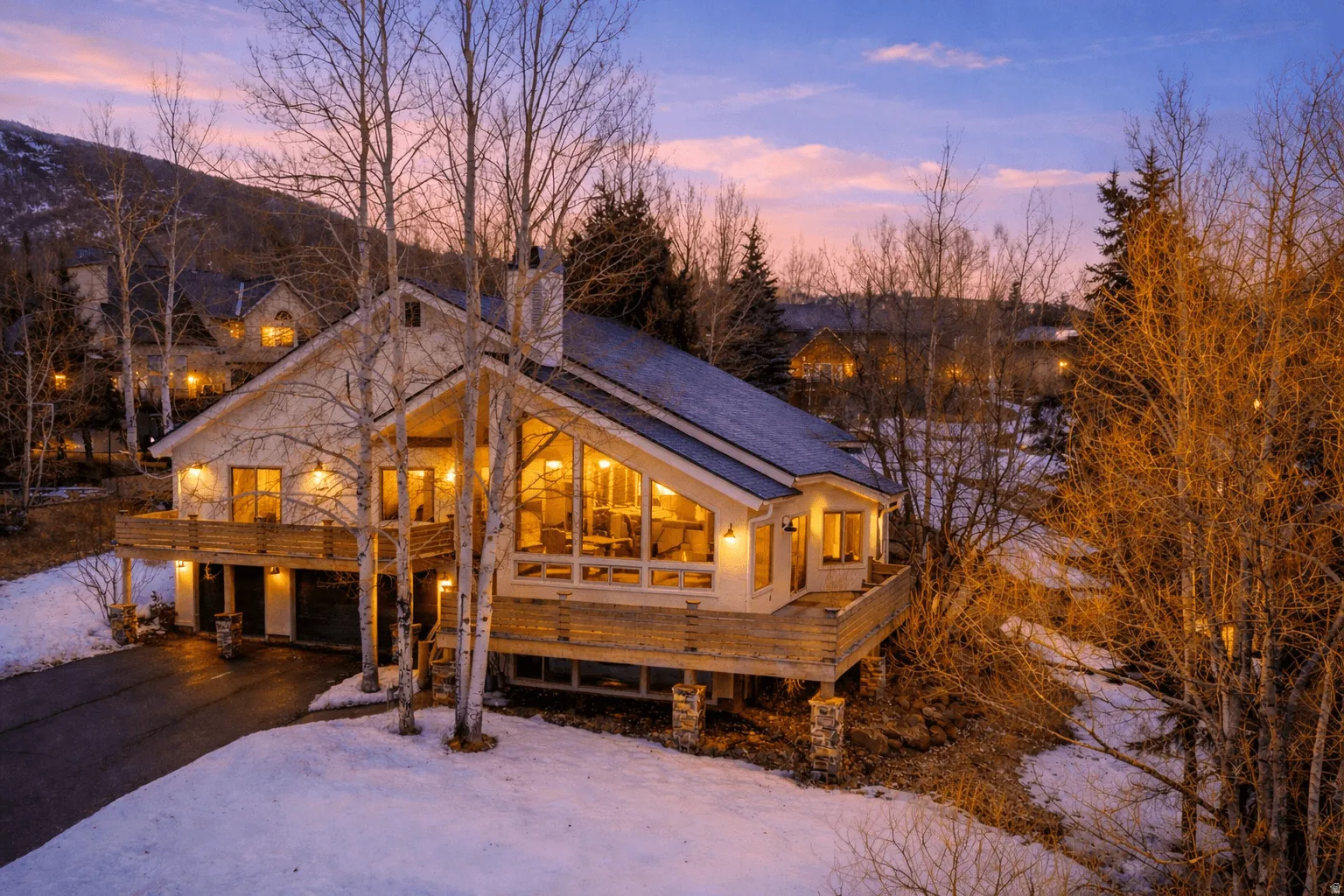 Contemporary mountain home with a striking A-frame architectural design, expansive windows, a prominent stone chimney, and an elevated wooden deck
