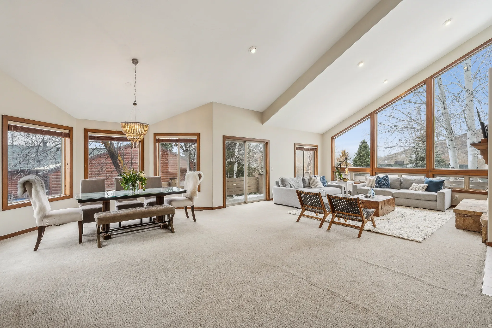 Vaulted ceilings with recessed lighting, expansive picture windows with wood framing, glass sliding door, light-toned carpeting, and a built-in fireplace mantel