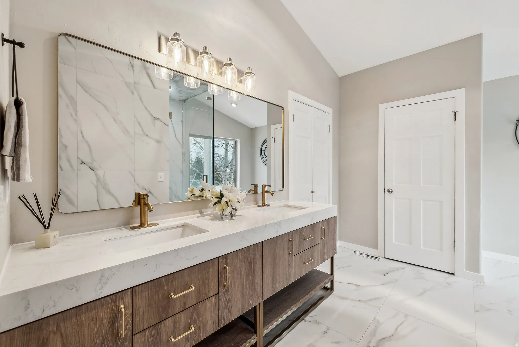 Dual sink vanity with wood-finish cabinetry, white countertop, and gold-finish fixtures