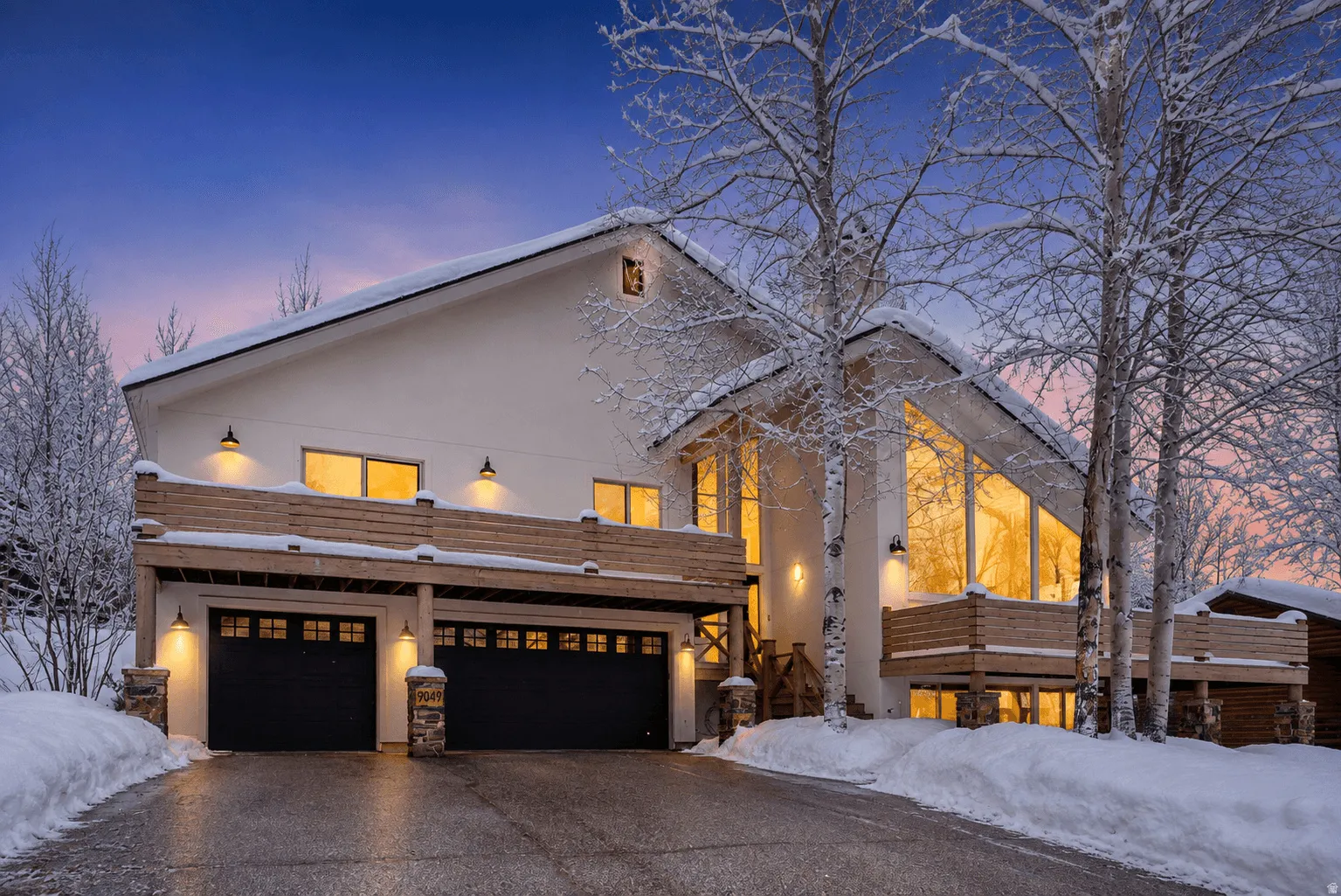 Modern architecture with a sloped roofline, expansive windows, two vehicle garage, and multiple exterior balconies