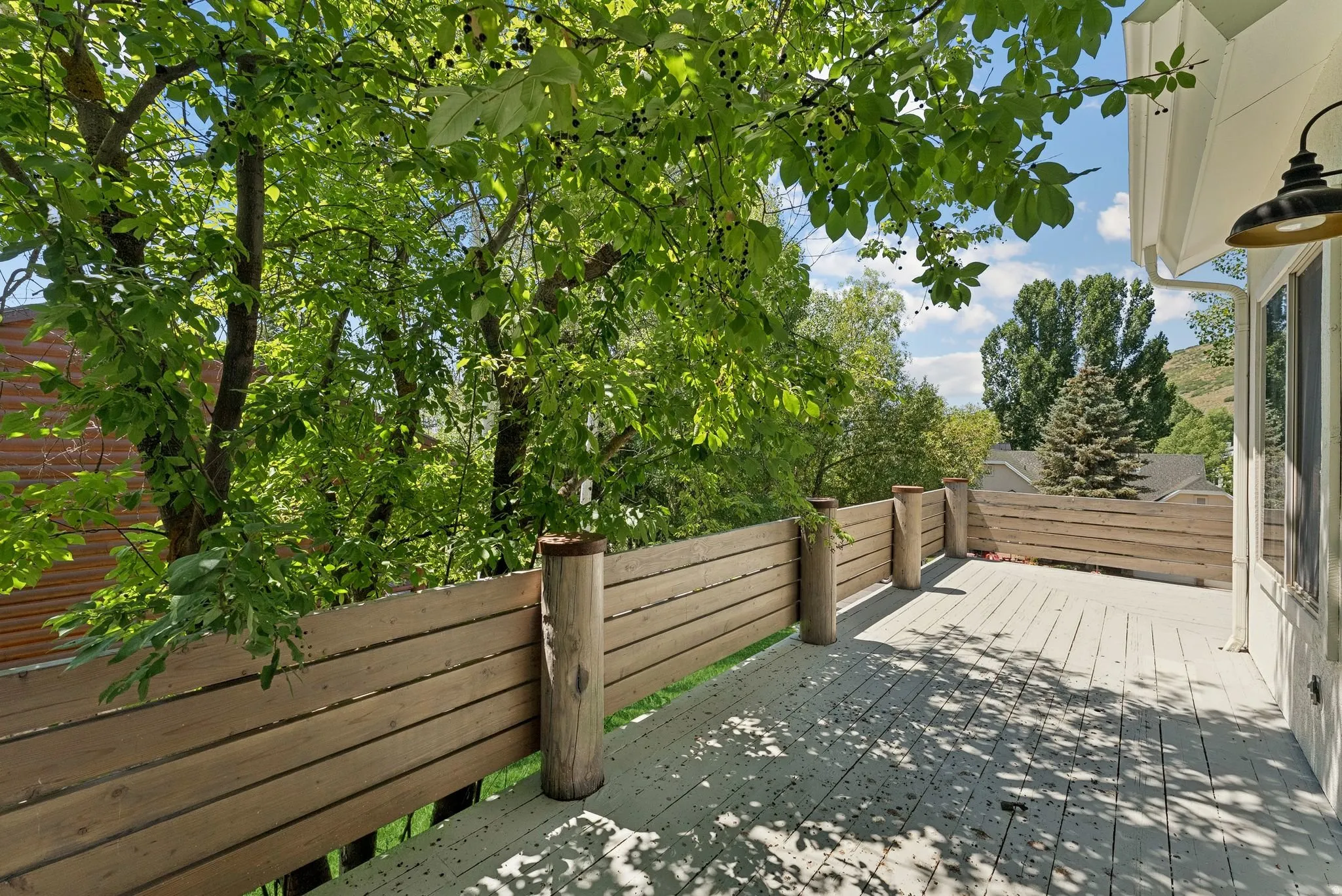 Expansive outdoor deck with wood privacy fencing, mature trees, and an exterior wall lantern