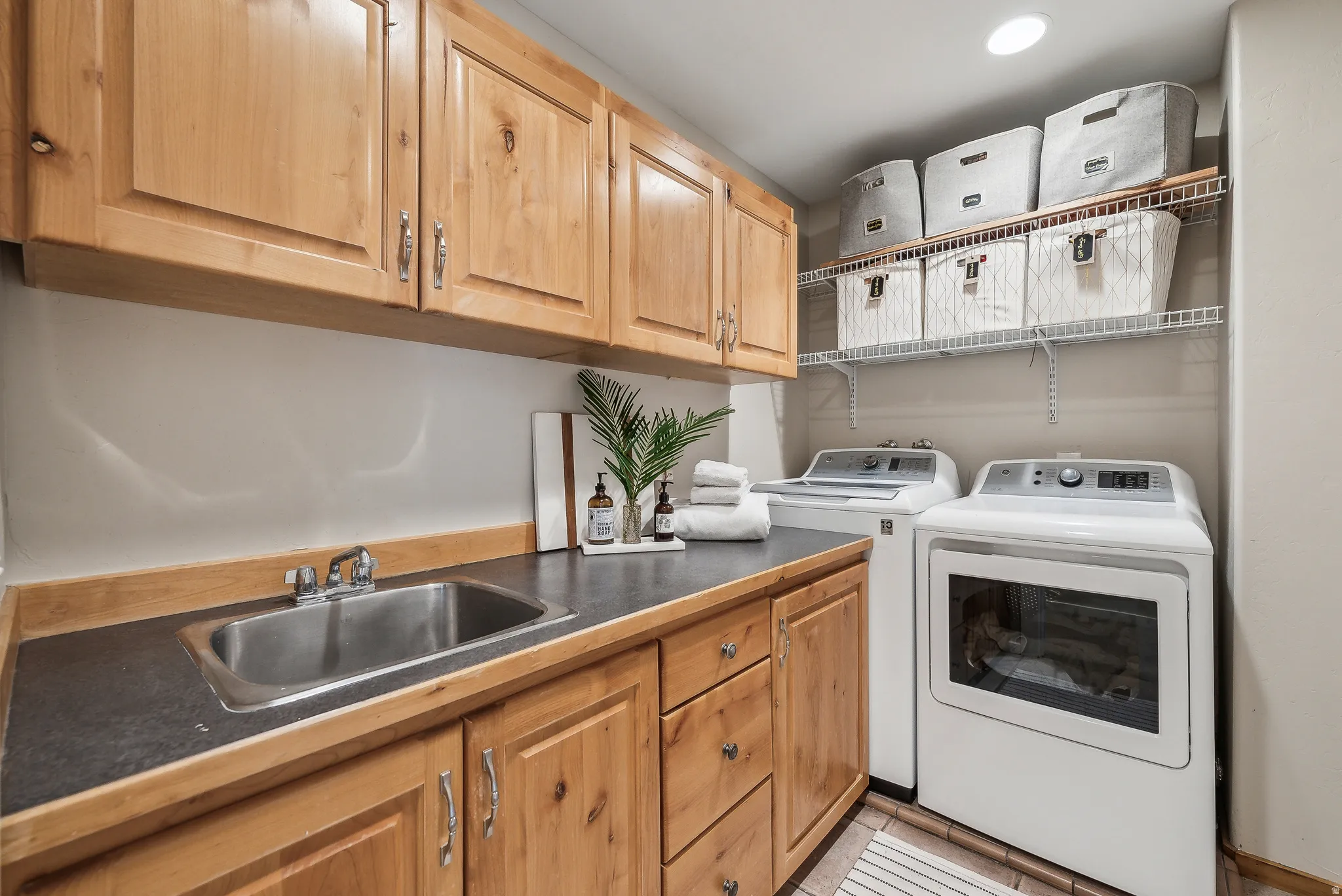 Built-in natural wood cabinetry, stainless steel sink, dark countertop, and overhead wire shelving