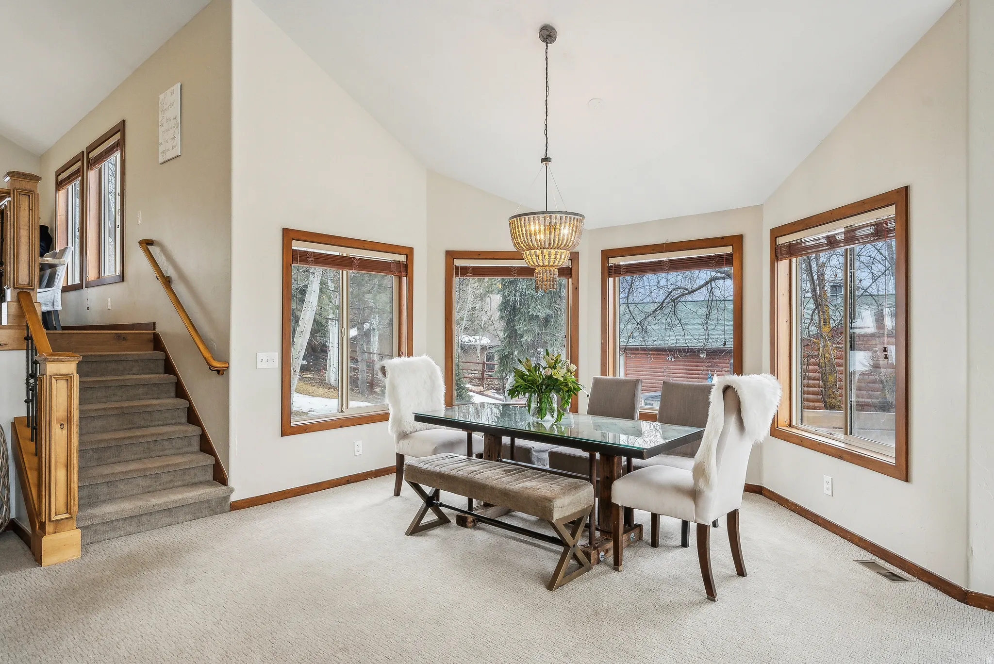 Carpeted dining space with stairs, a chandelier, and high vaulted ceiling