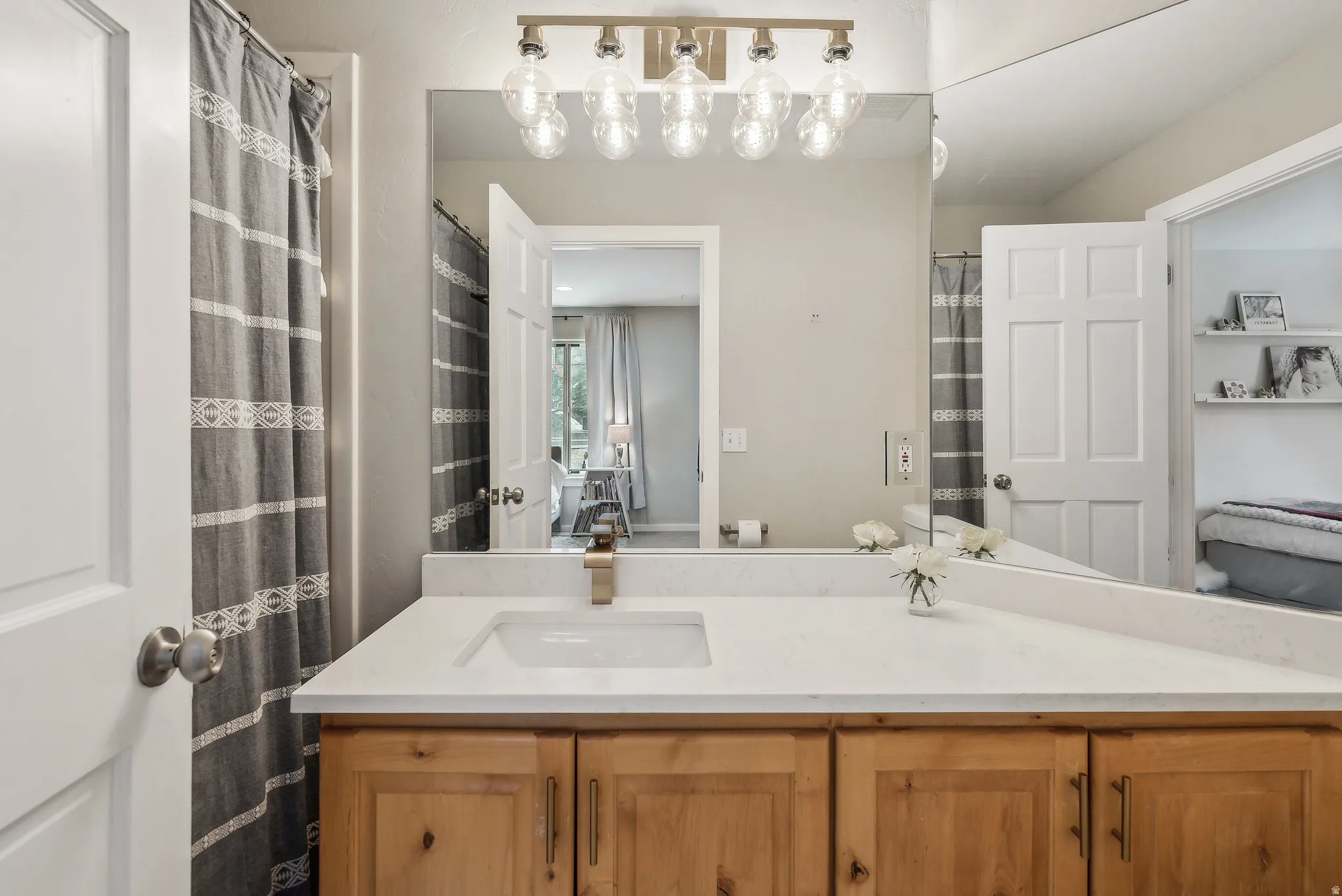 Bathroom featuring a wood-finish vanity with a single basin sink and light-toned countertop, illuminated by a multi-bulb vanity light fixture