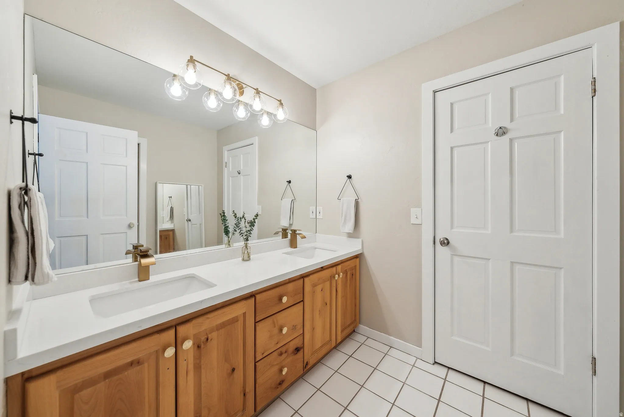 Dual vanity with integrated sinks, wood-finish cabinetry, a full-width mirror, and a multi-bulb light fixture