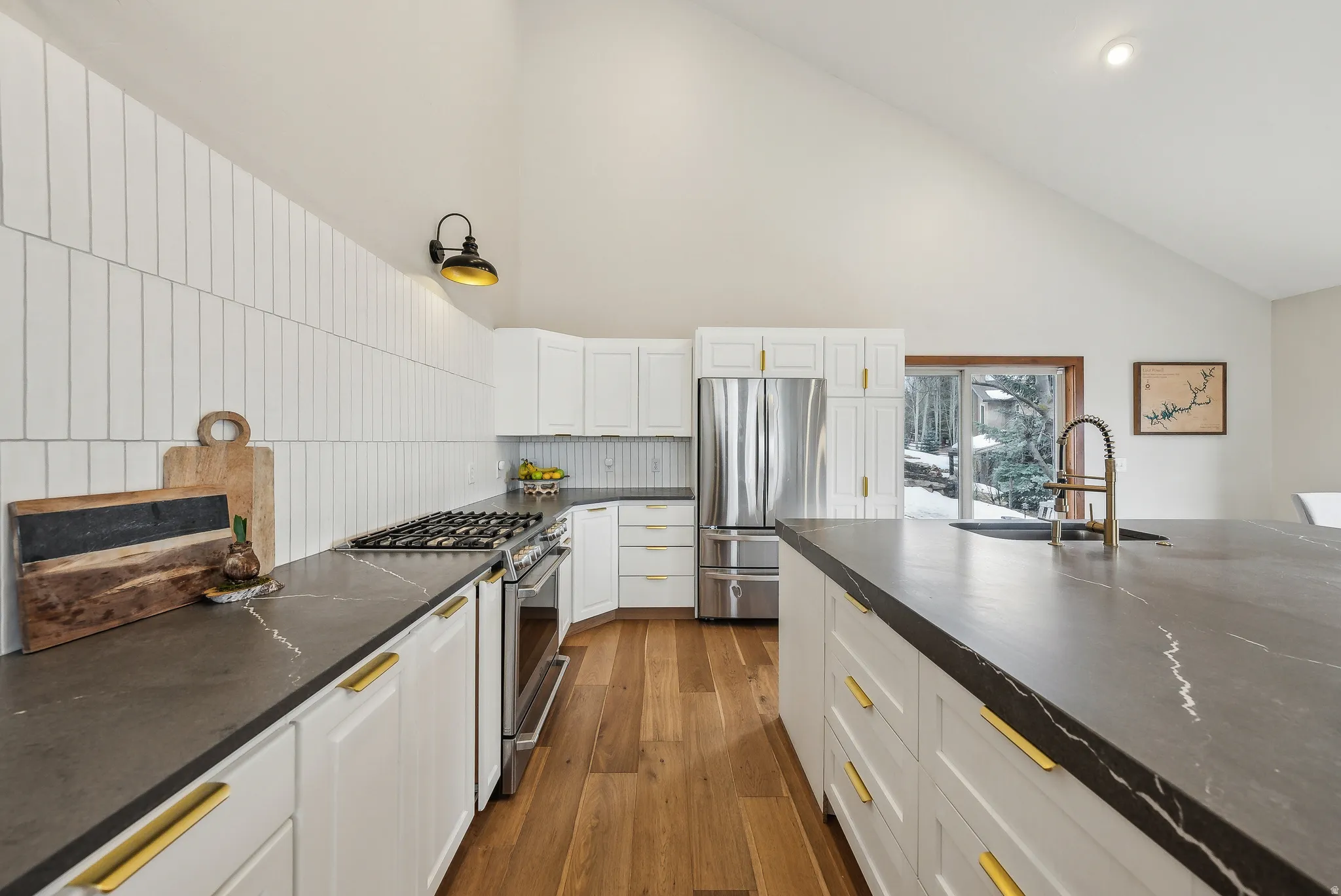 Vaulted ceiling kitchen featuring white cabinetry, dark countertops, wood-finish flooring, and a stainless steel gas range