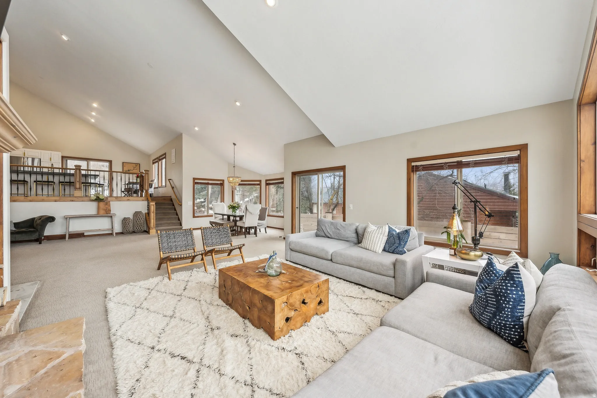 Vaulted ceilings with recessed lighting, stone fireplace, wood-frame windows, and a raised dining area