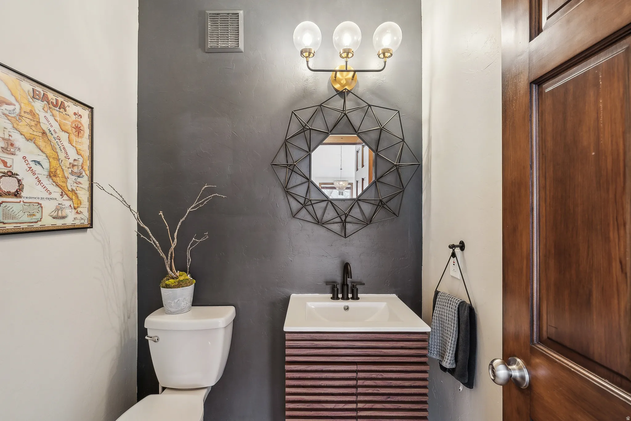 Wood-finish vanity with a rectangular sink, matte black faucet, and a decorative geometric mirror