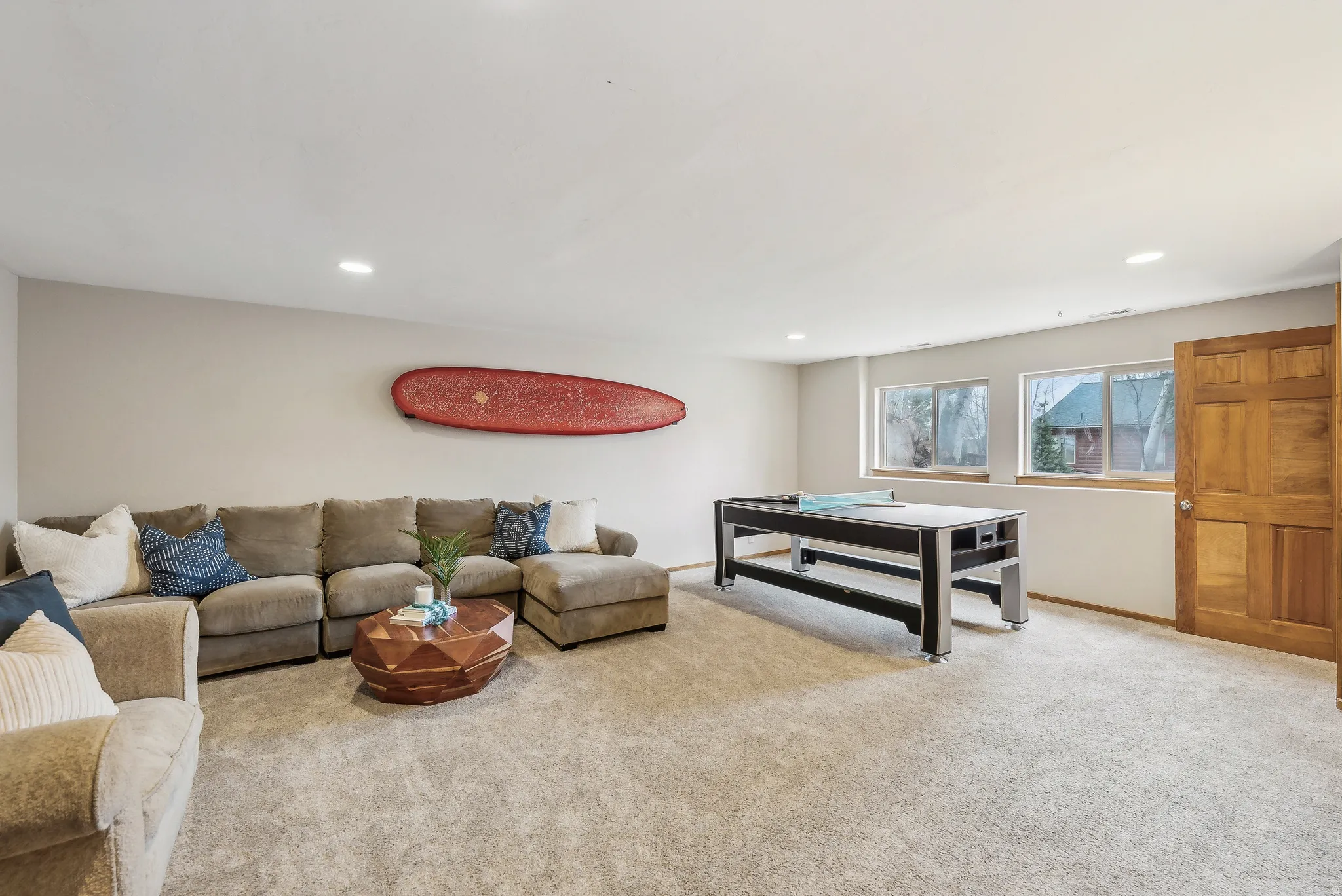 Spacious room featuring neutral carpeting, recessed lighting, multiple windows with wood trim, and a paneled wood door