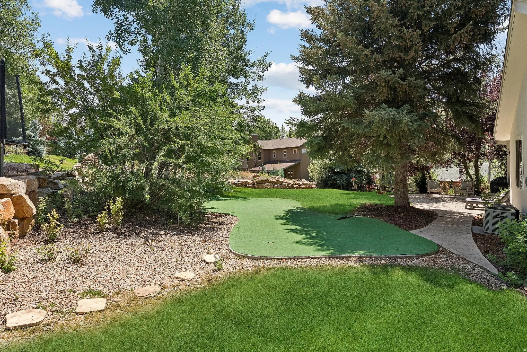 Expansive backyard with a putting green, mature trees, a natural stone retaining wall, a paved patio, and stepping stones