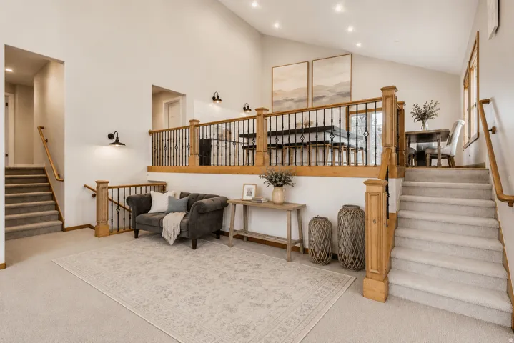 Vaulted ceilings, a carpeted staircase with wood handrails, and a second-story open railing with black spindles