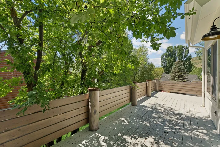 Expansive outdoor deck with wood privacy fencing, mature trees, and an exterior wall lantern